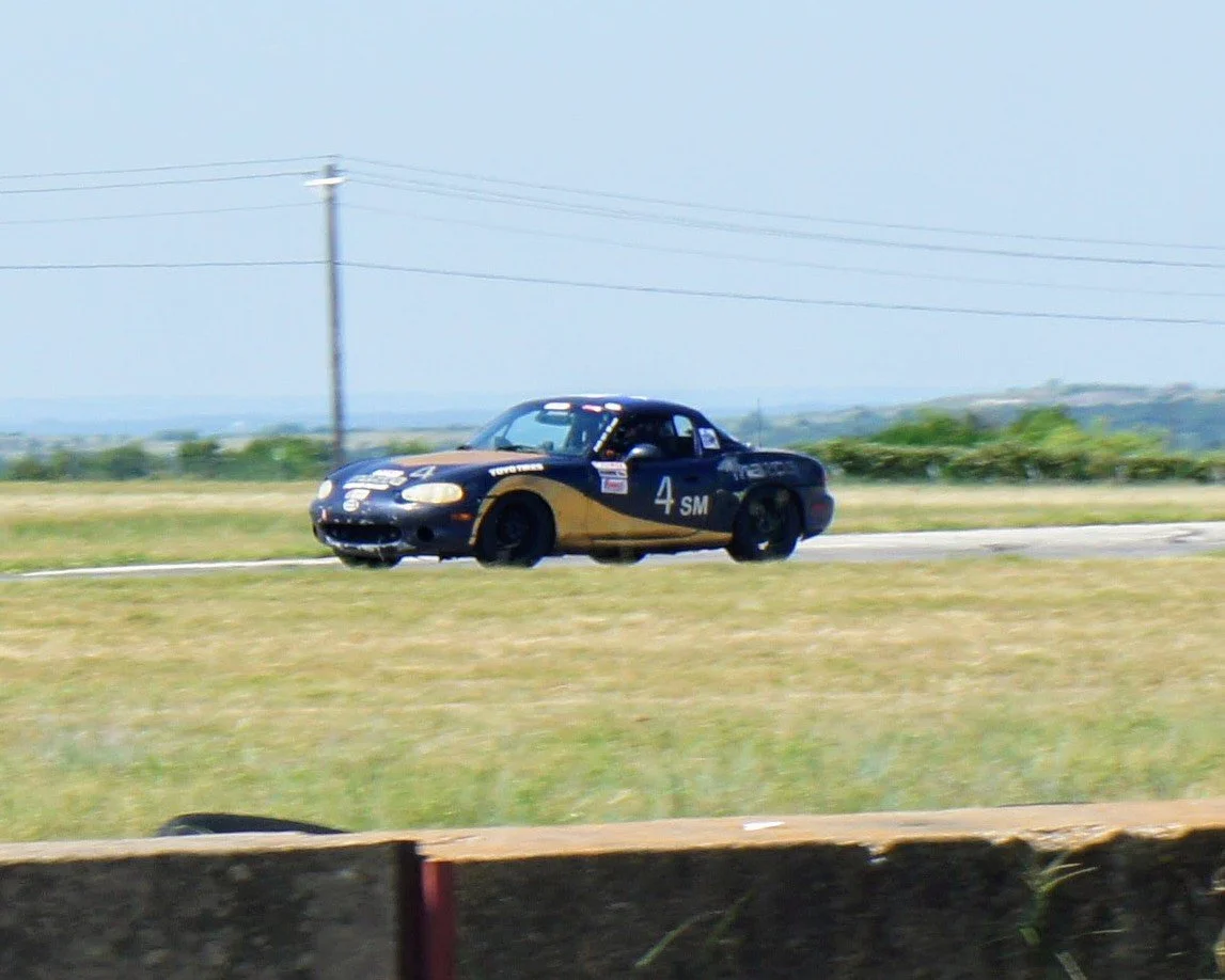A race car on a track during a race, with a blue sky and green landscape in the background.