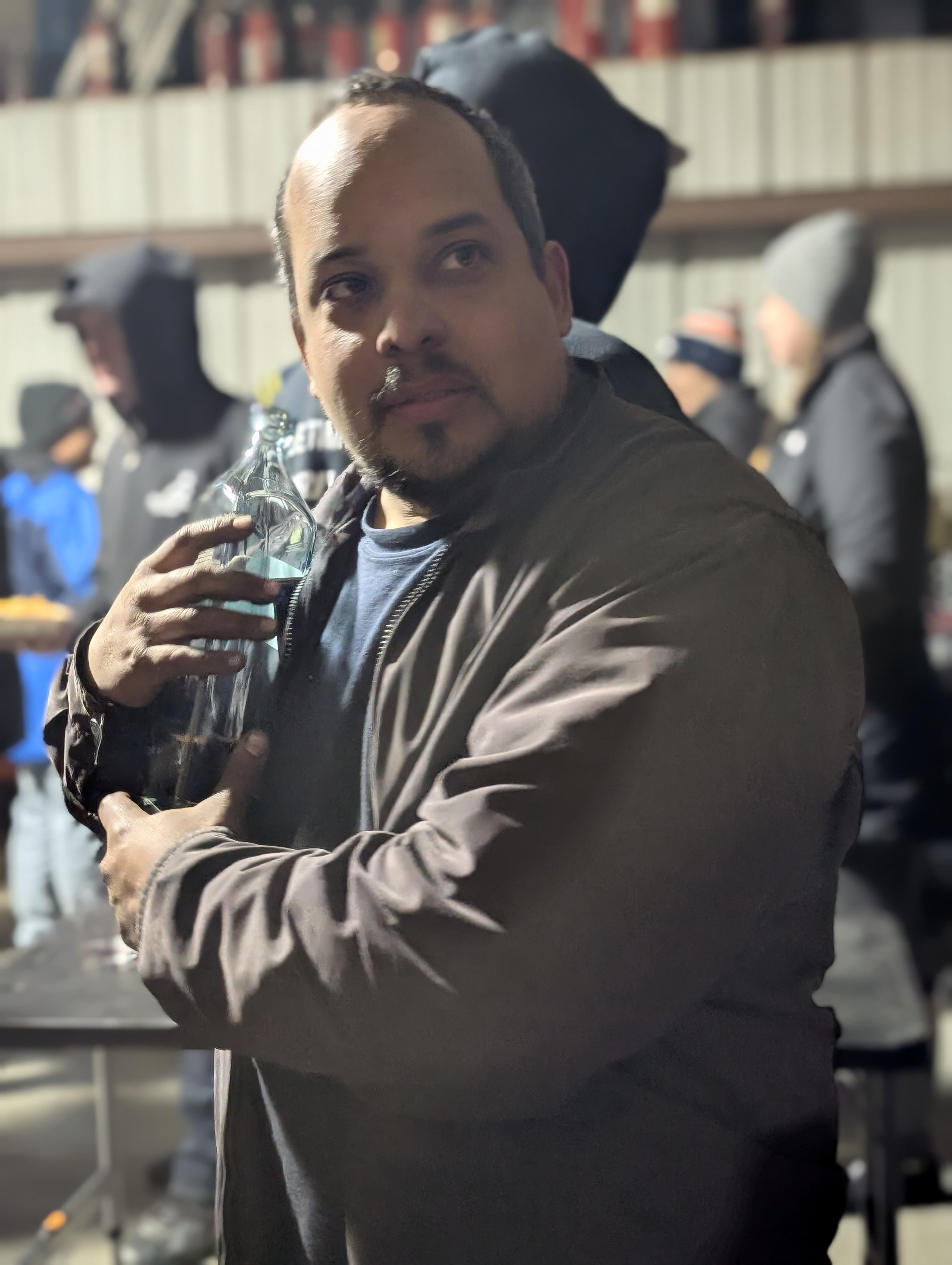 A man holding a glass bottle while standing with others in a social setting.