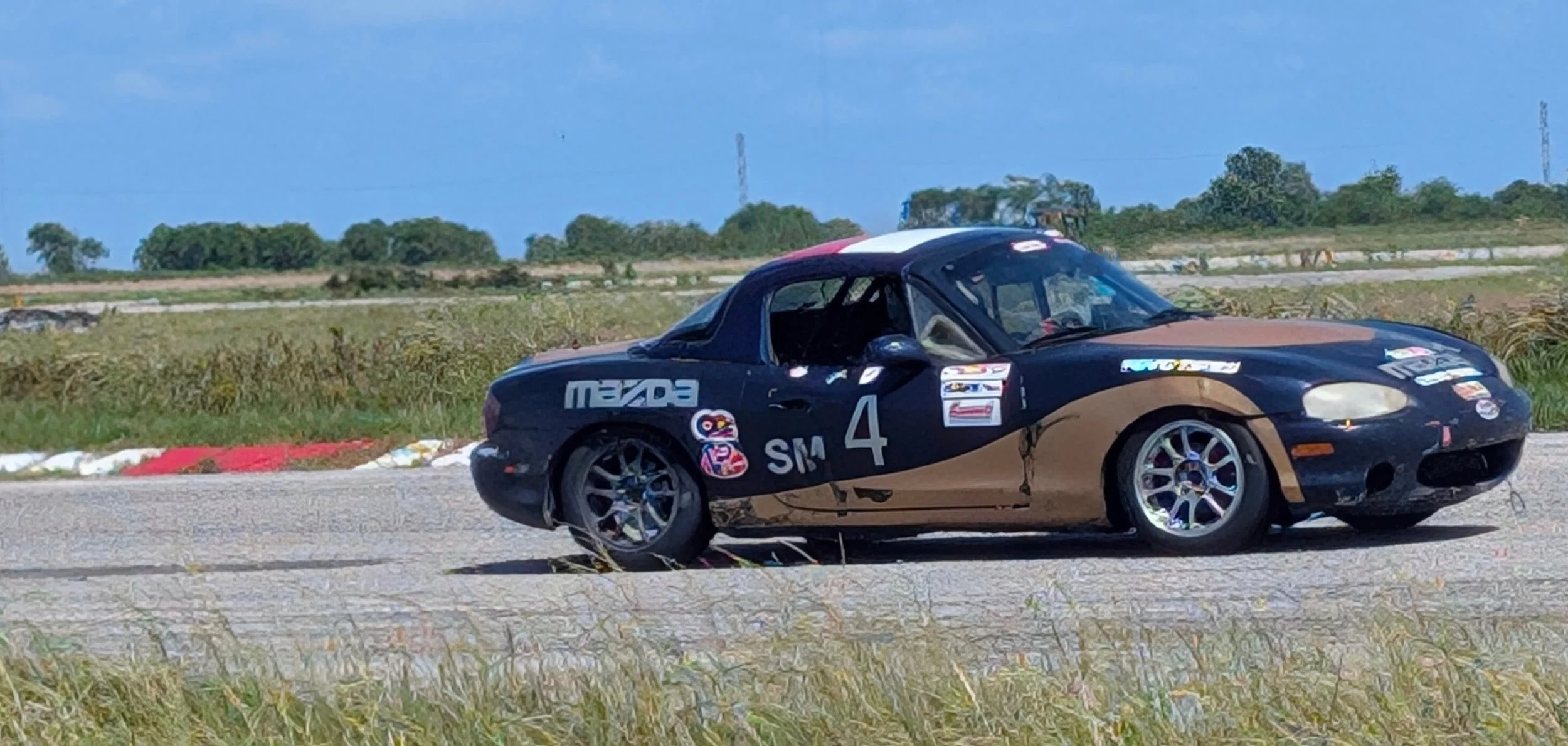 A race car on a track with a black and gold paint job and various sponsor decals, including Mazda and number 4.