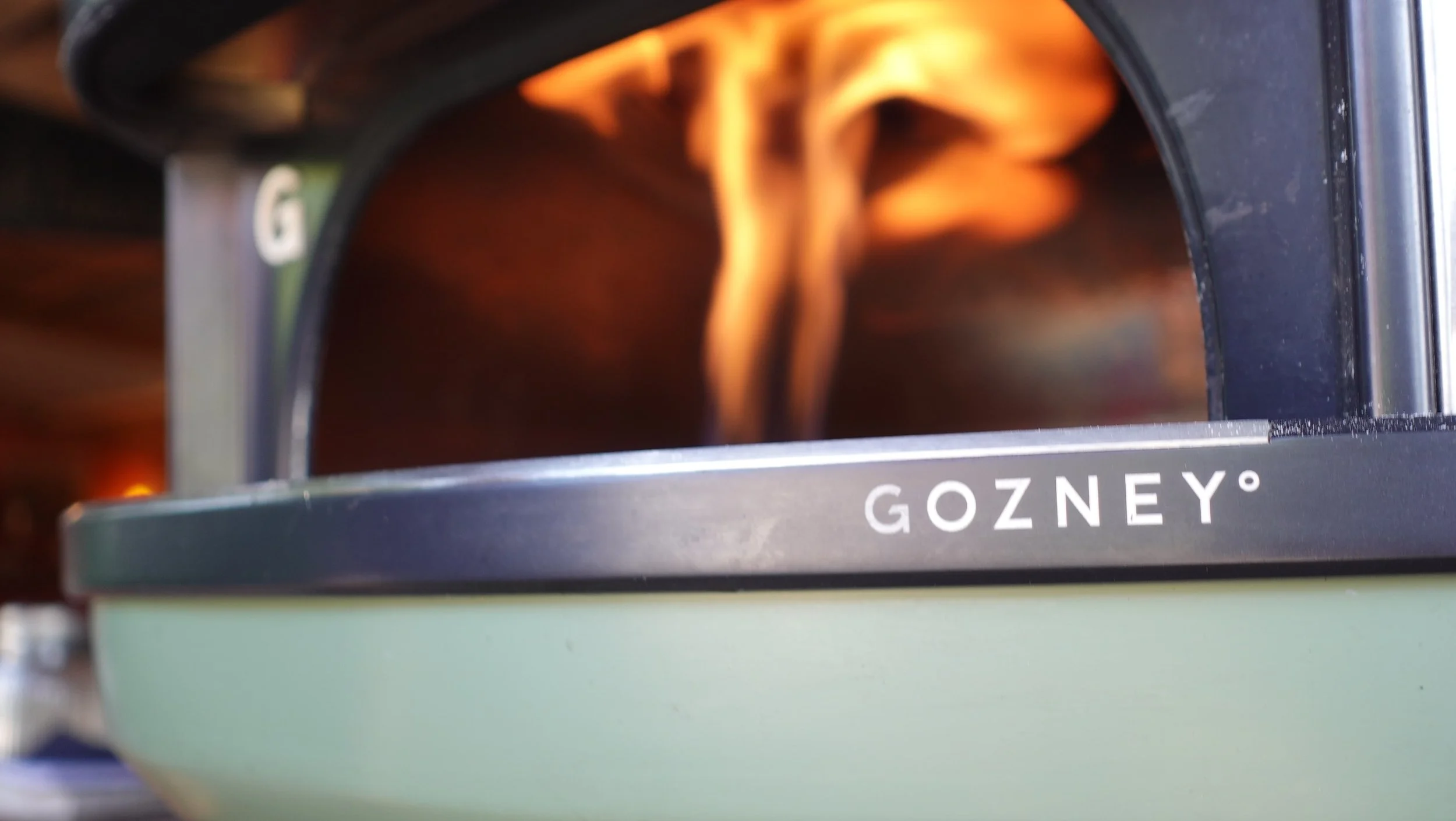 Close-up of a stove with a flame visible through an opening, branded with the name GOZNEY.