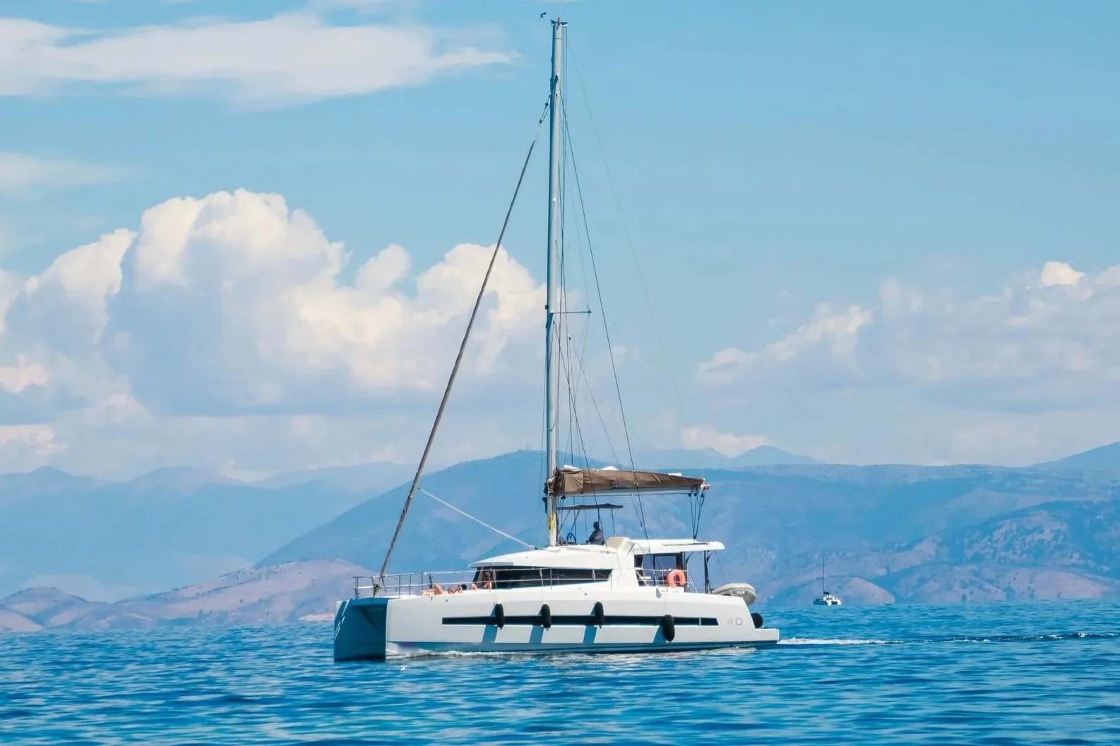 A sailboat on calm blue waters with mountains in the background and a partly cloudy sky.