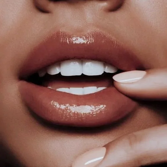 Close-up of a person's lips slightly parted, showing white teeth and a finger touching the lower lip.