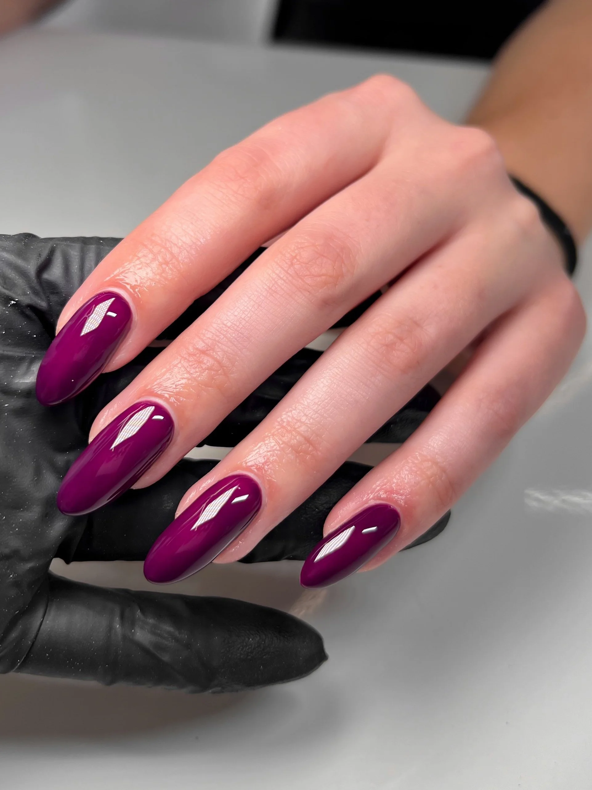 Close-up of a hand with manicured BIAB nails painted in a glossy deep purple color.