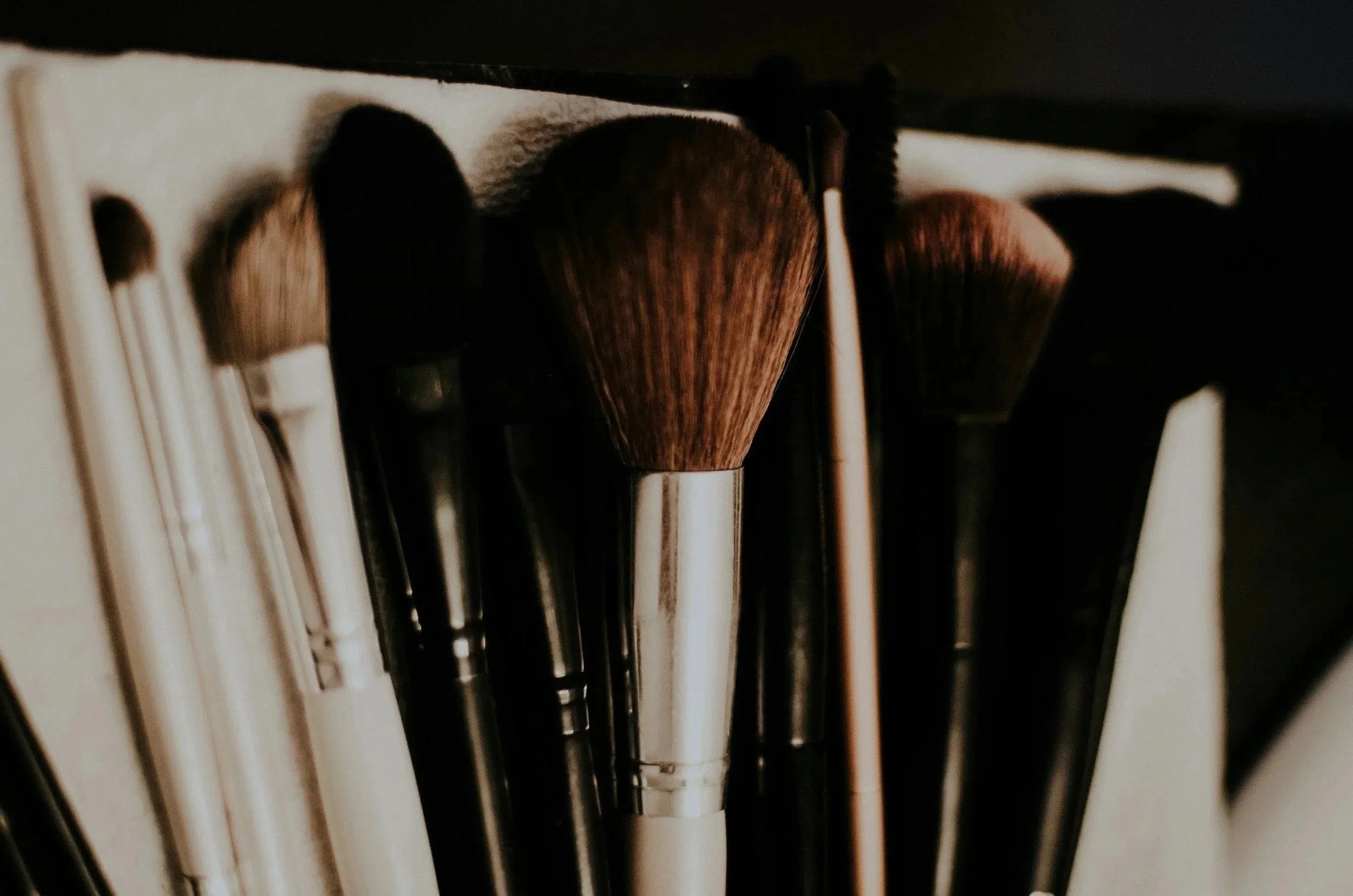 Close-up of various makeup brushes stored in a container with a dark background.