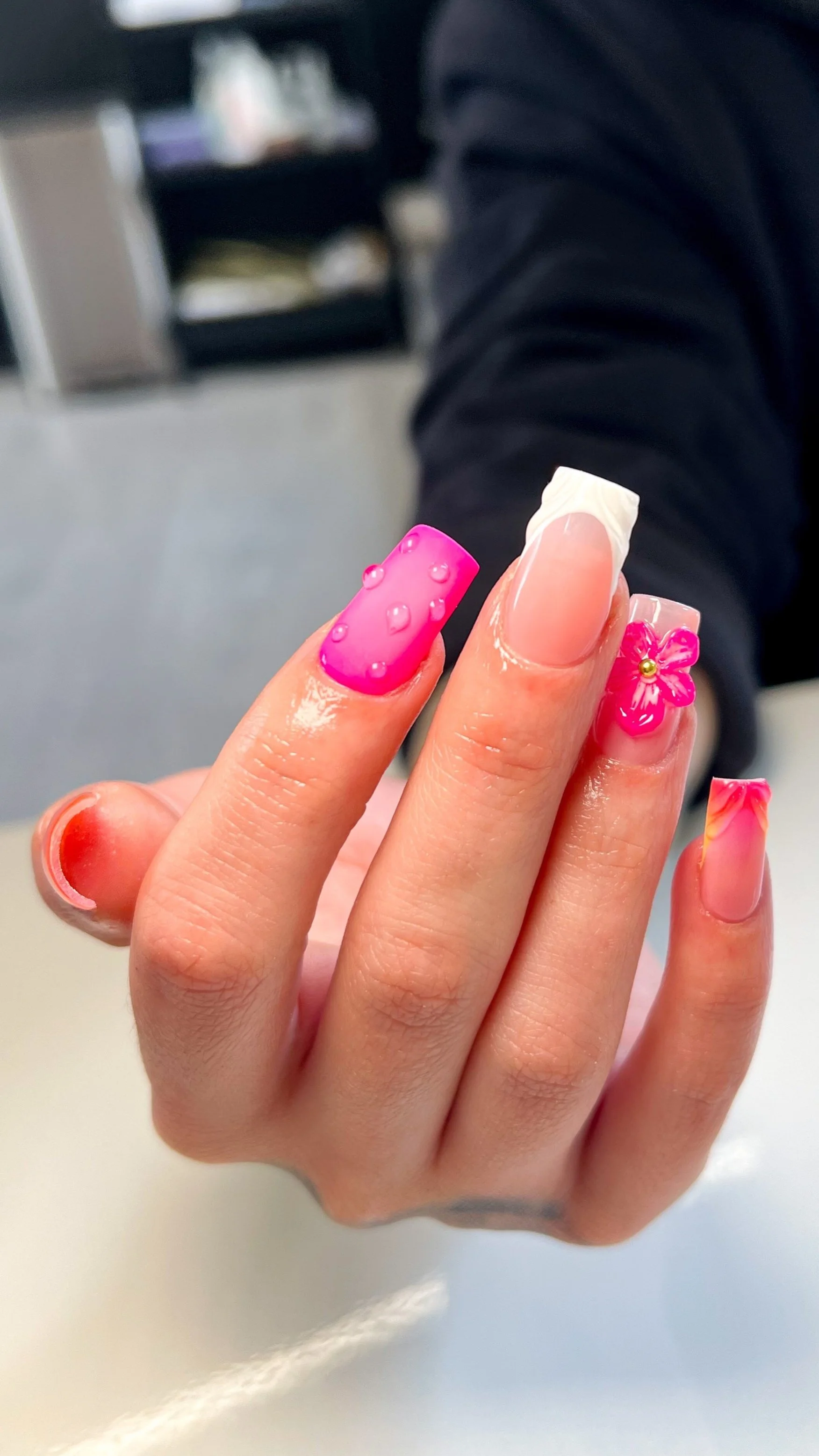 Close-up of a person's hand showing GELX manicured nails with pink, clear, and floral designs.