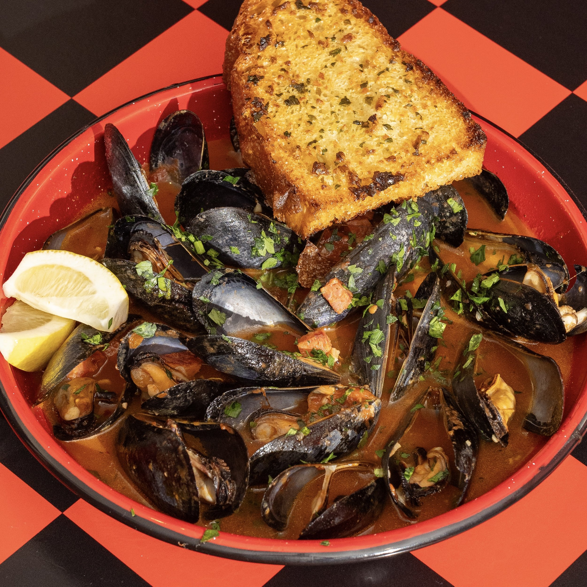 A bowl of clam chowder garnished with chopped herbs, served with lemon wedges and a piece of toasted garlic bread on top.