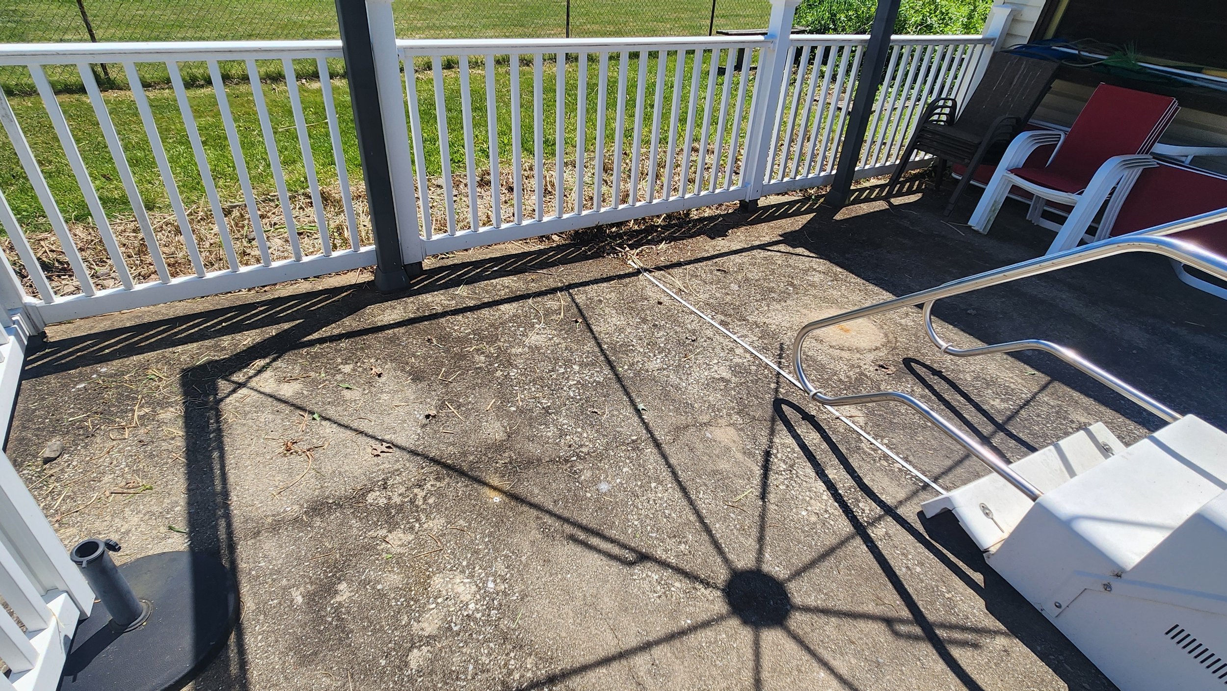 Back patio with stacked chairs, a white railing, and a cluttered outdoor space before being cleaned.