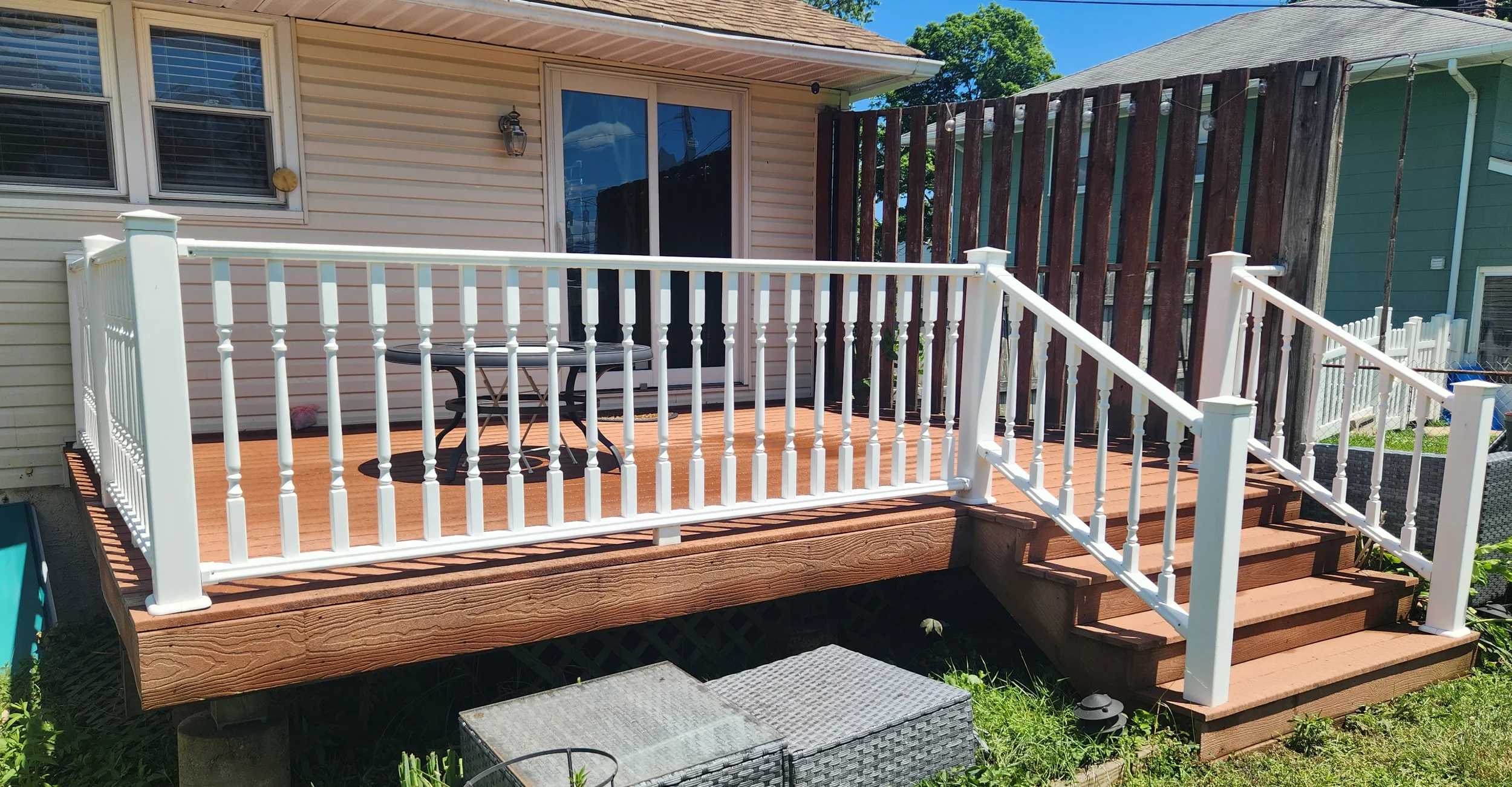 A backyard wooden deck with white railings, stairs, and a black round table with matching chairs. Railings are bright white after being cleaned.