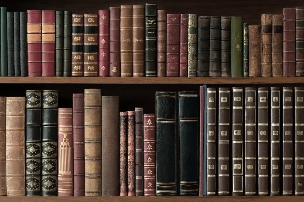 Bookshelf filled with vintage books lined in rows, featuring leather-bound volumes in various colors including brown, red, and green.