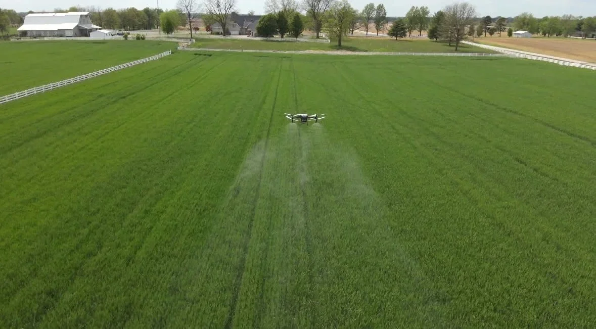 A drone flying over a green farm field on a sunny day.