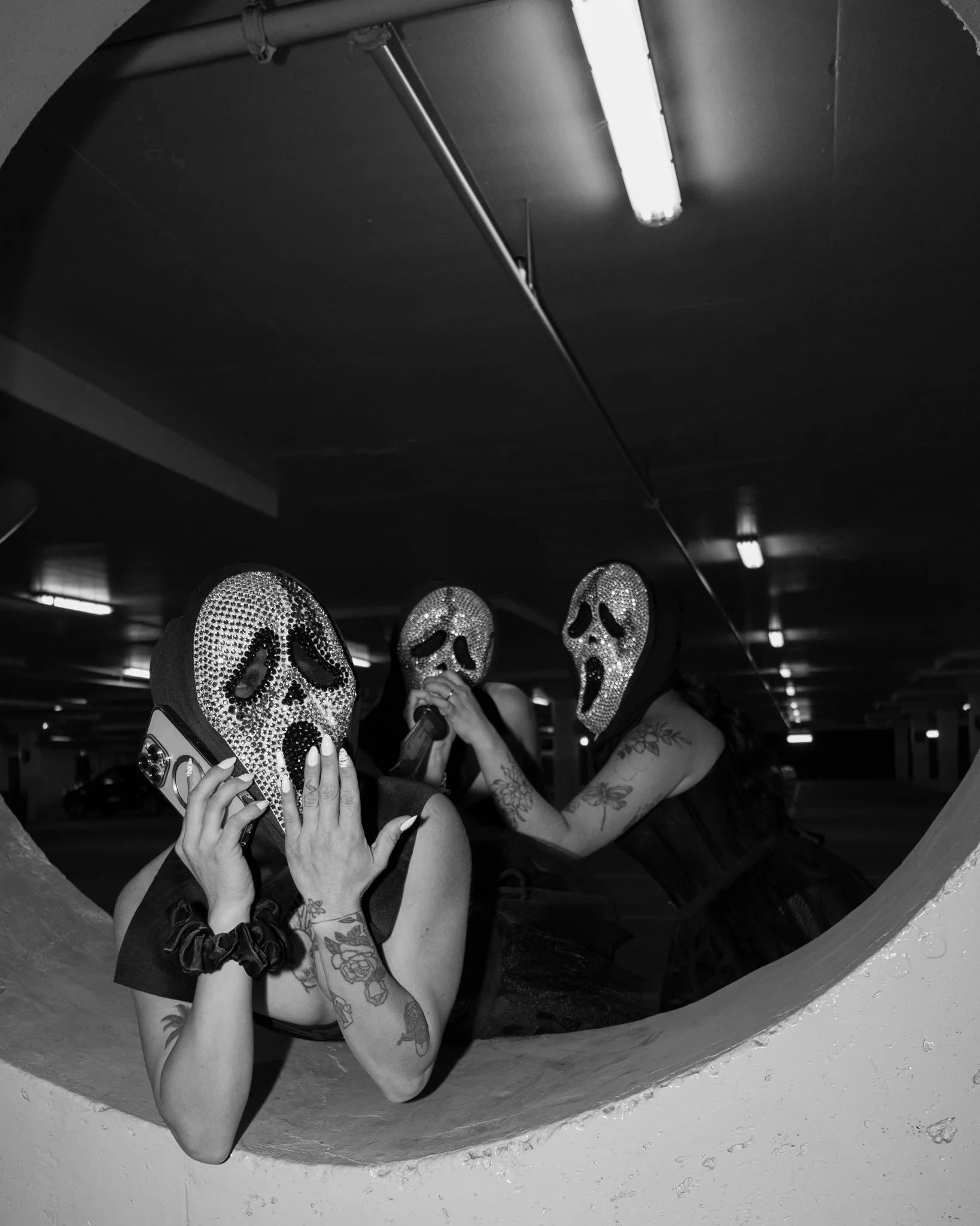 Three people wearing Halloween masks with sequin skull designs, in a dark parking garage, three are posing through a circular opening in a wall.