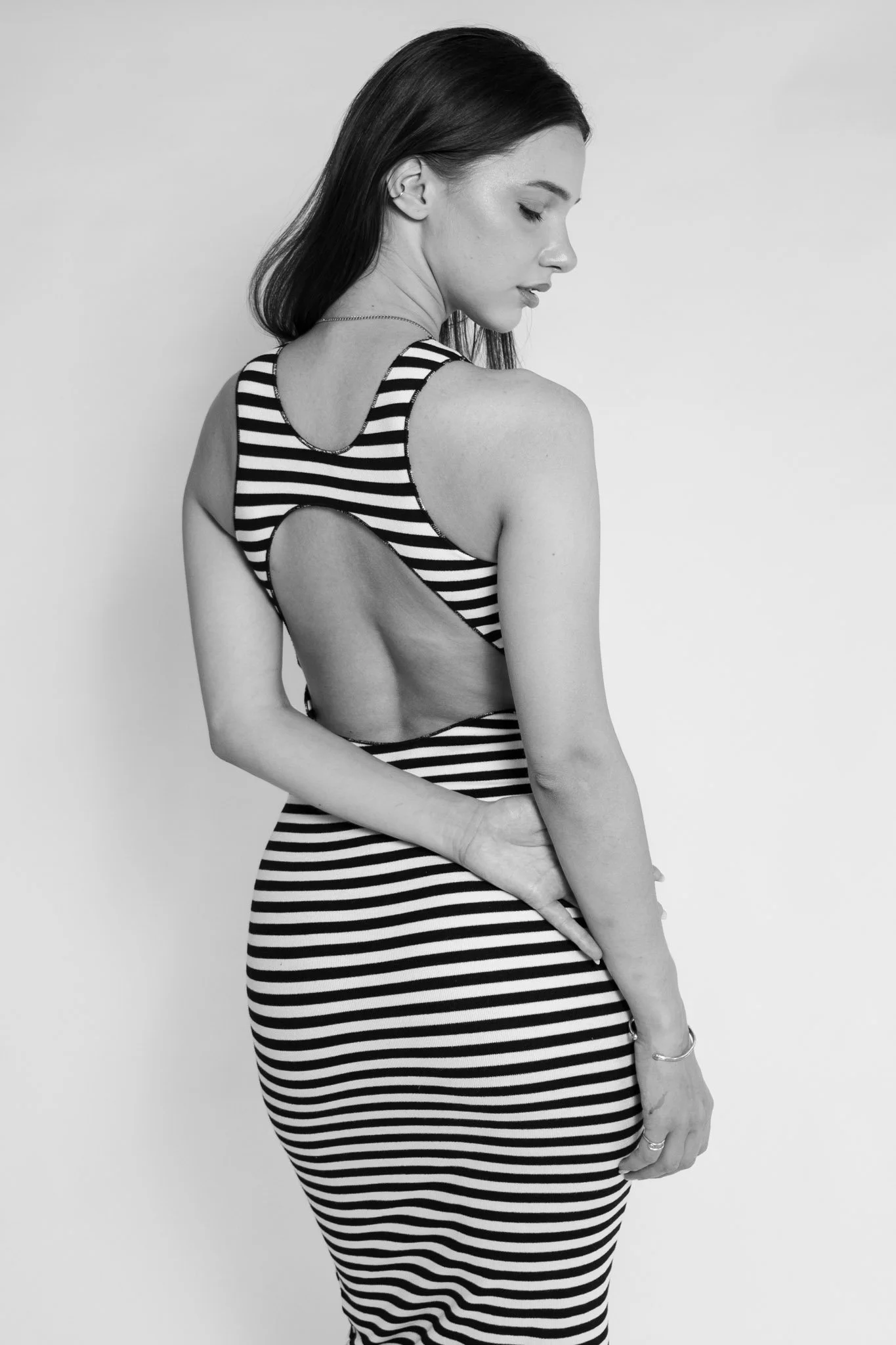 A woman in a striped dress with cutout on the back, posing with her eyes closed and looking downward.