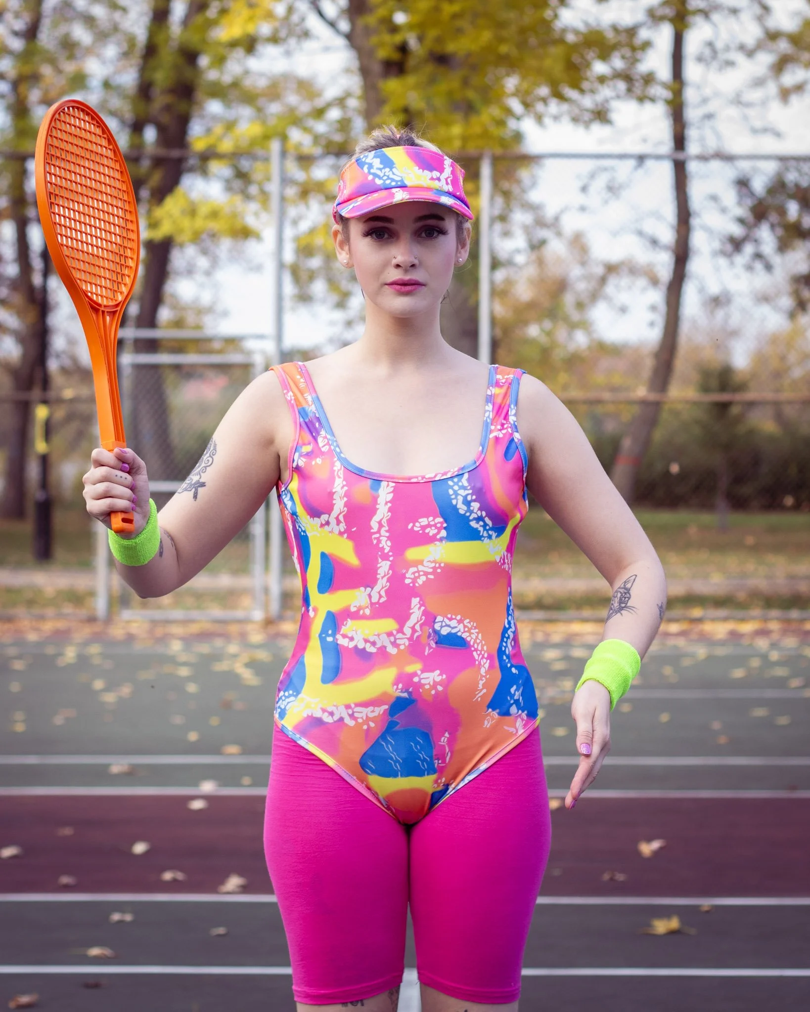 Woman holding a tennis racket on a tennis court surrounded by autumn trees.