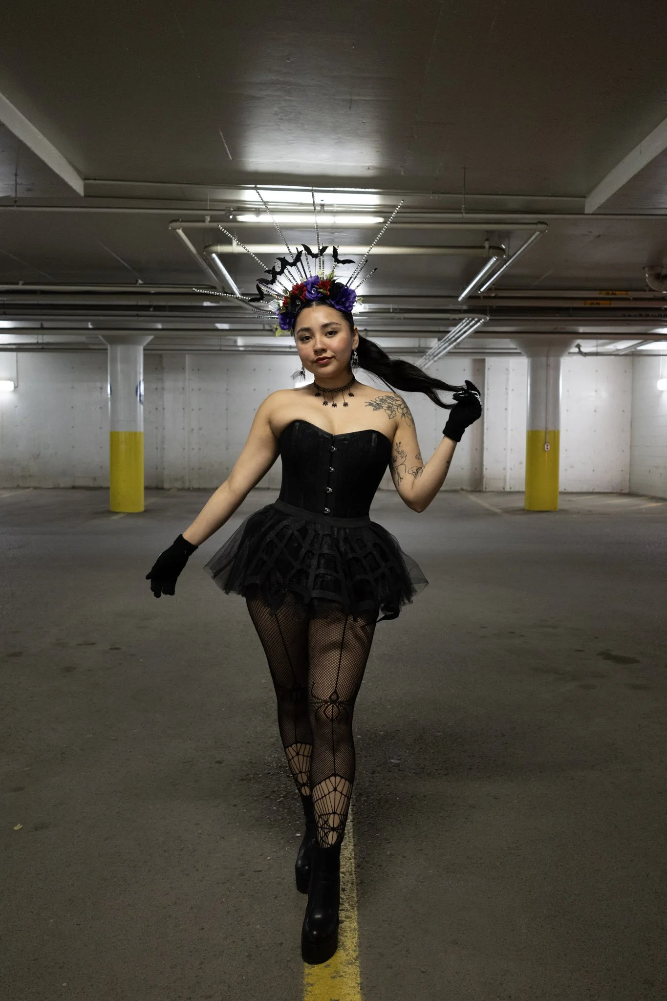 Woman in black corset, tutu, fishnet stockings, and platform boots standing in an empty parking garage.