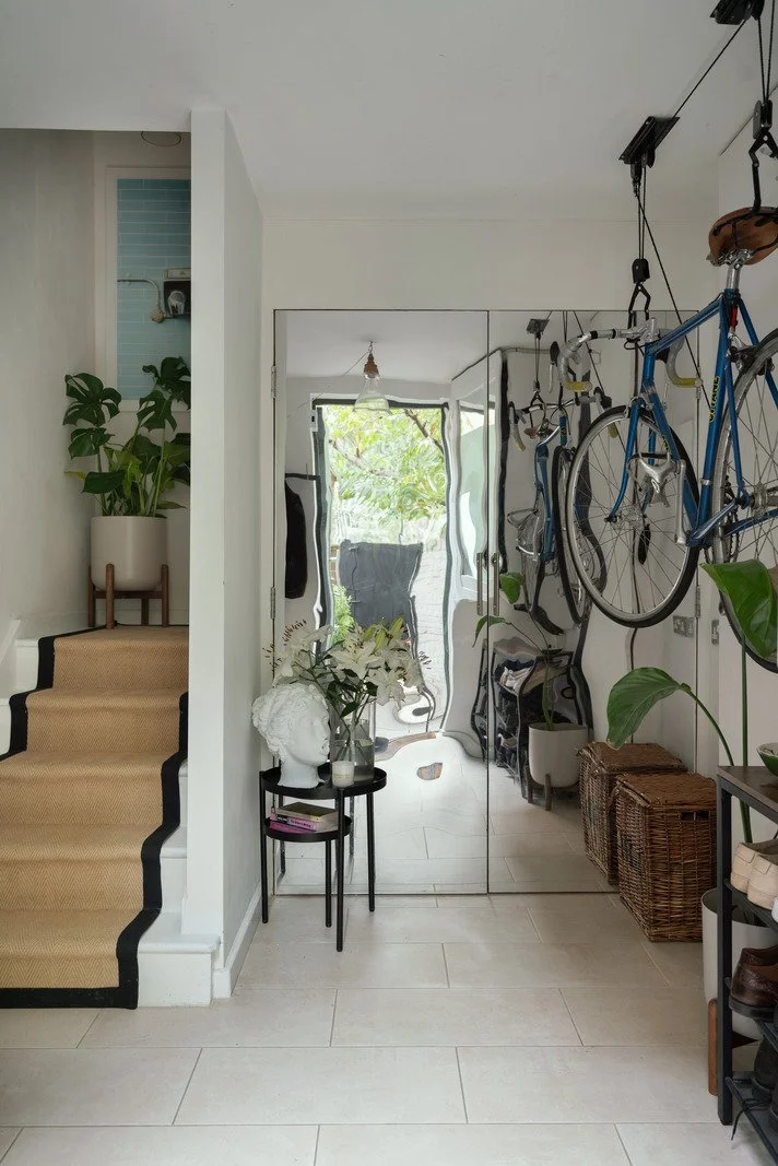 Interior of a home entrance with a mirror closet, bicycles hanging from the ceiling, a staircase with a beige runner, and various plants and decorative items.