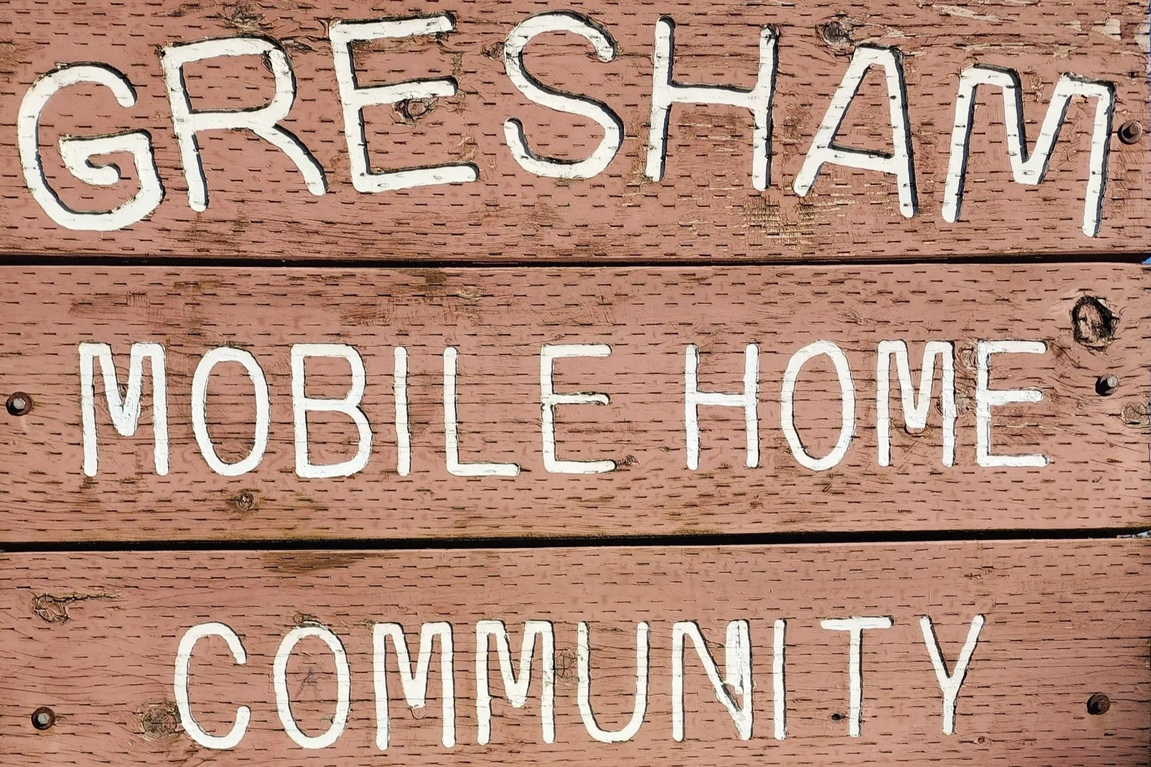 Wooden sign with white painted text that reads 'GRESHAM MOBILE HOME COMMUNITY'.