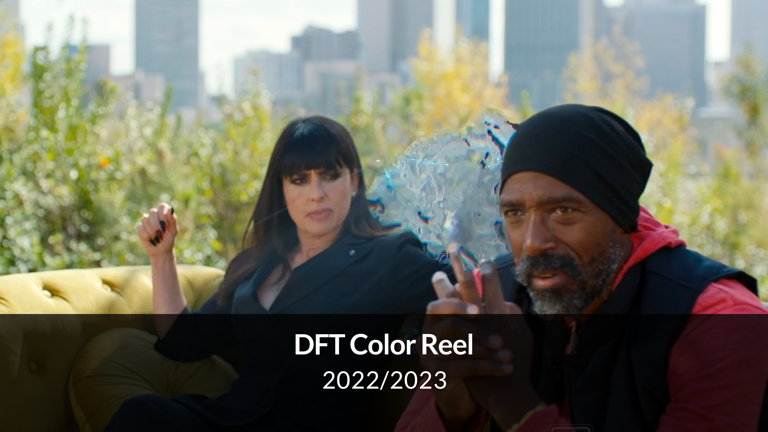 A woman with long dark hair and a man with a black beanie sitting on a yellow couch outdoors with cityscape and trees in the background, a holographic projection floating between them.