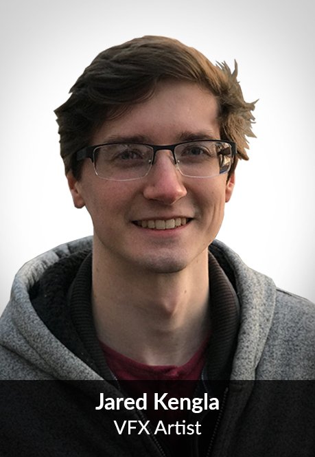 A young man with brown hair, glasses, and a smile, wearing a gray hoodie with a black inner lining, standing against a plain light background.