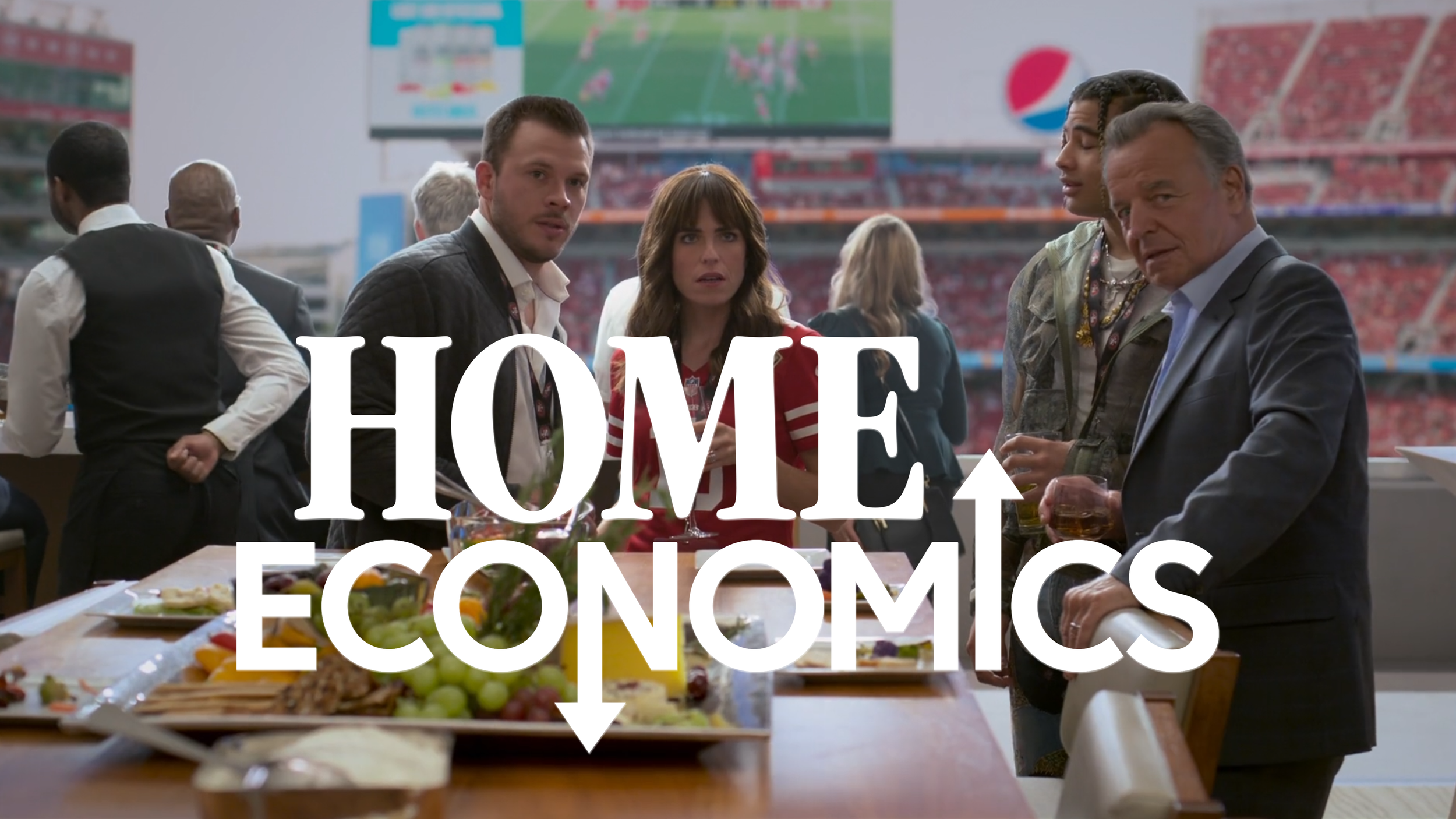 People at a social gathering in a sports stadium, with food and drinks on the table, and a large screen displaying a football game in the background, during a reception or party related to the game.