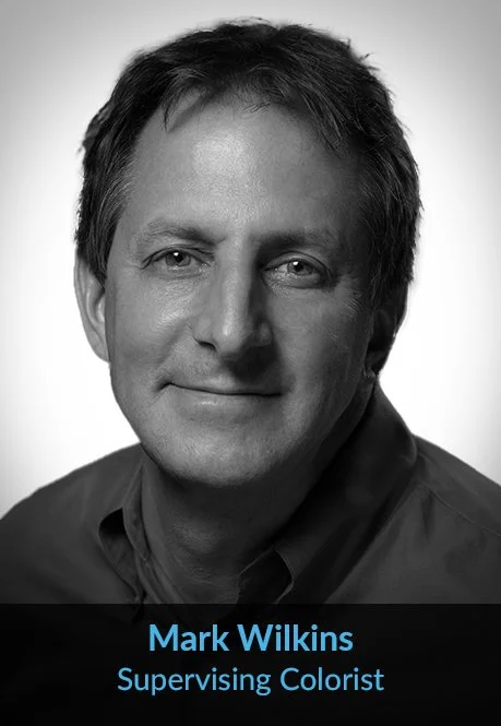 Black and white headshot of a man with short dark hair, wearing a collared shirt, smiling slightly. Text at the bottom reads "Mark Wilkins, Supervising Colorist."