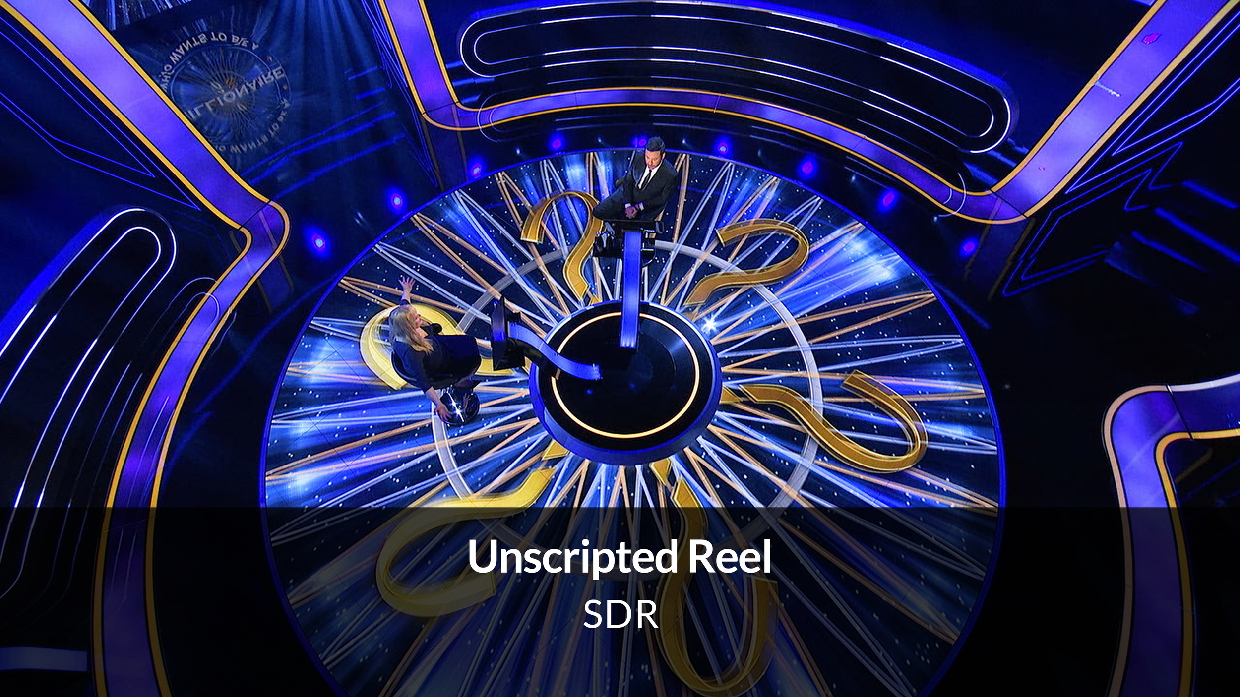 Two people sit on chairs attached to a wheel resembling a large clock with glowing numbers, as part of a game show set with blue and gold lighting and futuristic design.