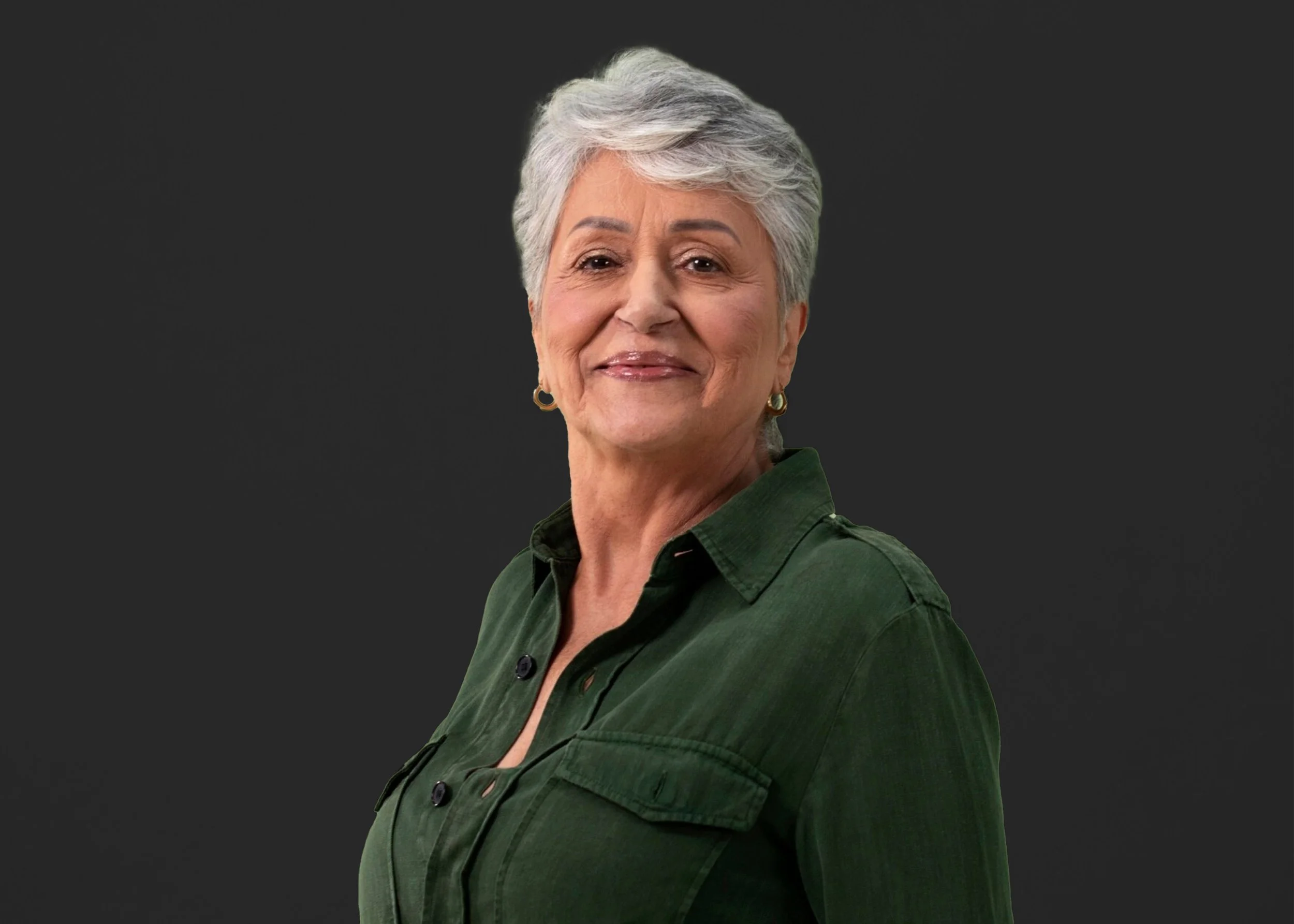 Older woman with short gray hair smiling, wearing a dark green shirt with a dark background.