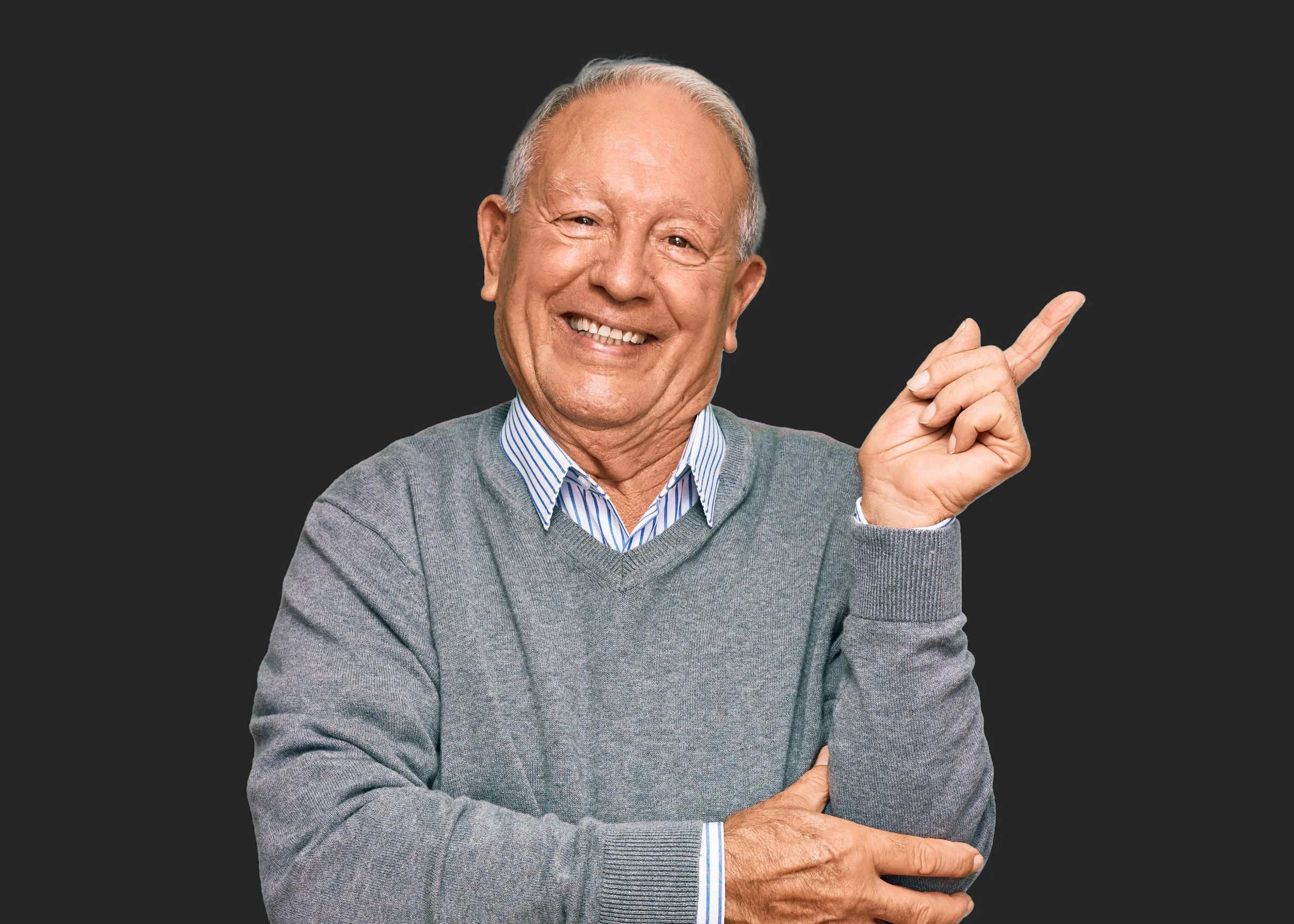 Elderly smiling man wearing a gray sweater and striped shirt, pointing to his right.