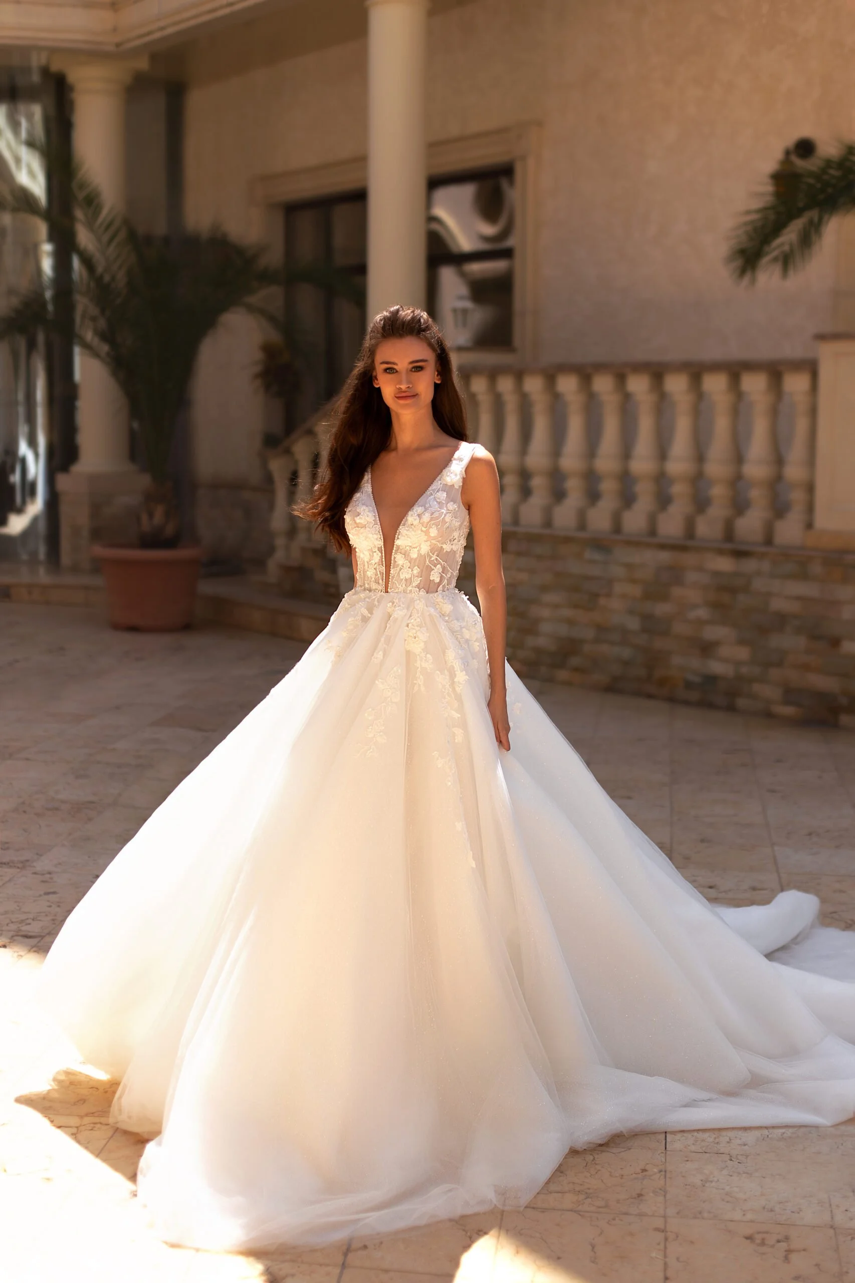 A woman in a white wedding gown standing outdoors on a marble patio with columns and potted plants.