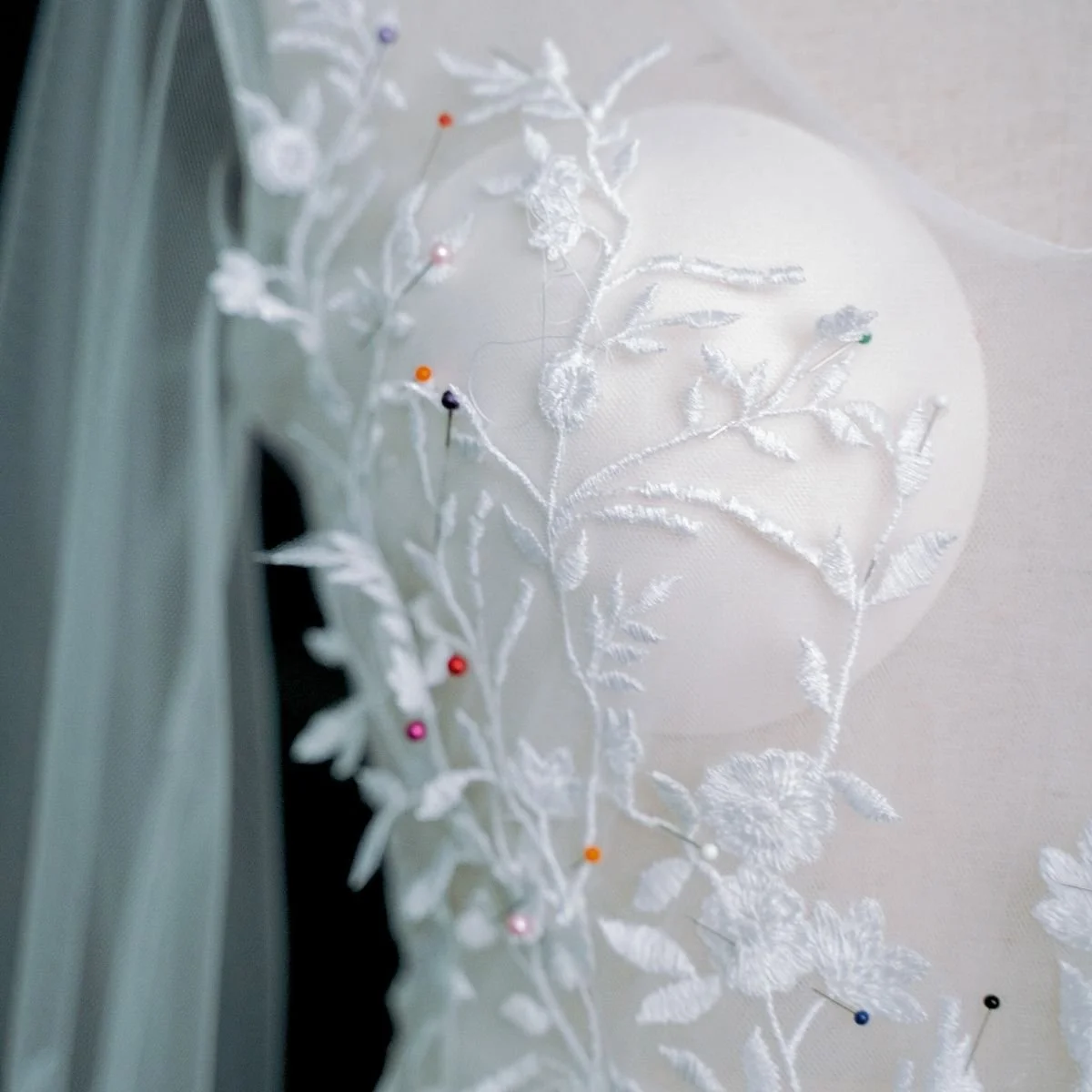 Close-up of white embroidered lace fabric with colorful straight pins, with a blurred background.