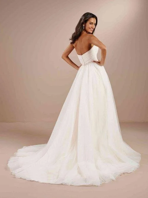 Woman in a white strapless wedding dress with a full train, smiling and posing with her hands on her hips.