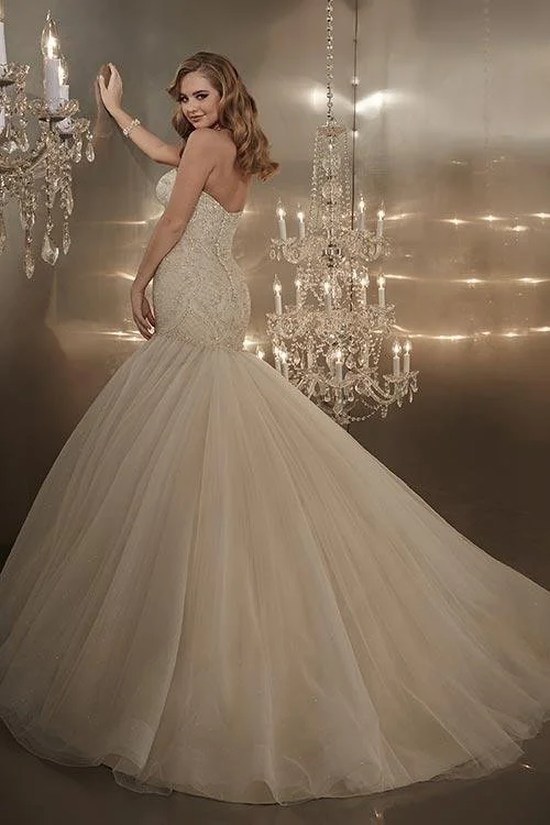 A woman wearing a strapless, intricately beaded wedding dress with a fitted bodice and a full, flowing tulle skirt, standing next to a chandelier in an elegant setting.