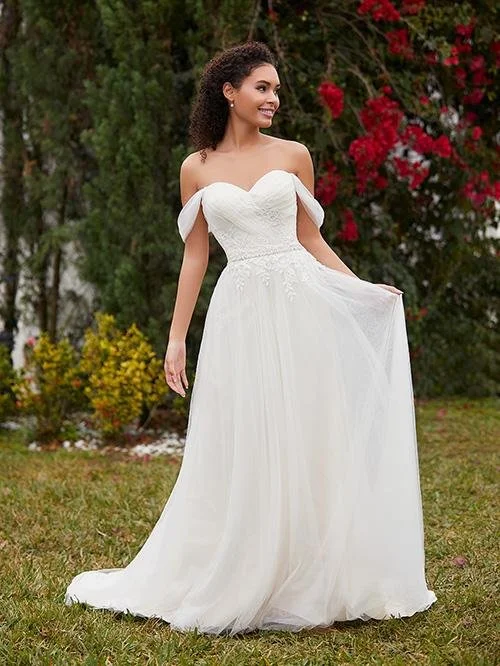 Young woman in a white strapless wedding dress with off-the-shoulder sleeves standing outdoors in a garden with red and yellow flowers.