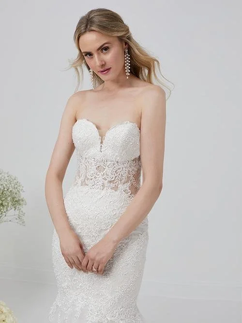 A young woman in a white lace wedding dress with a strapless sweetheart neckline, standing against a plain light gray background.