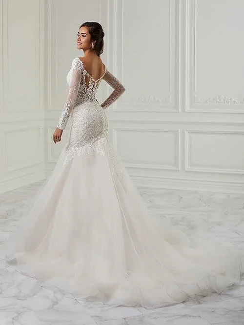 A woman in a white, long-sleeved lace wedding dress standing in a room with white paneled walls and marble floor.