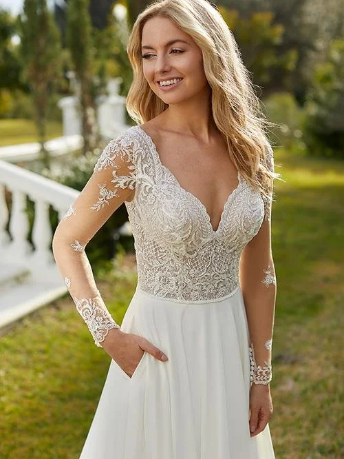 A woman in a white lace wedding dress standing outdoors on a sunny day.