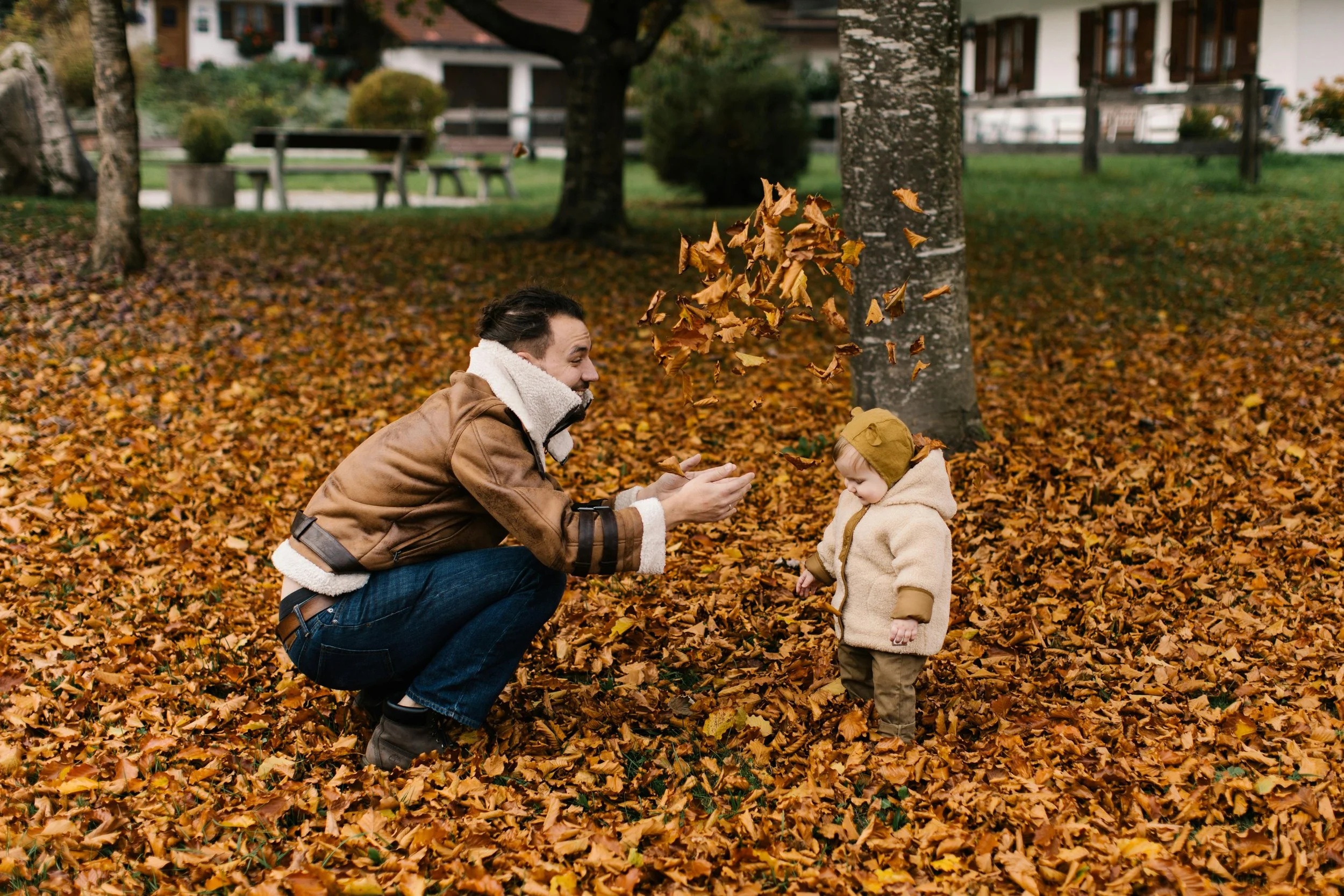 A young child playing in the leaves with a parent