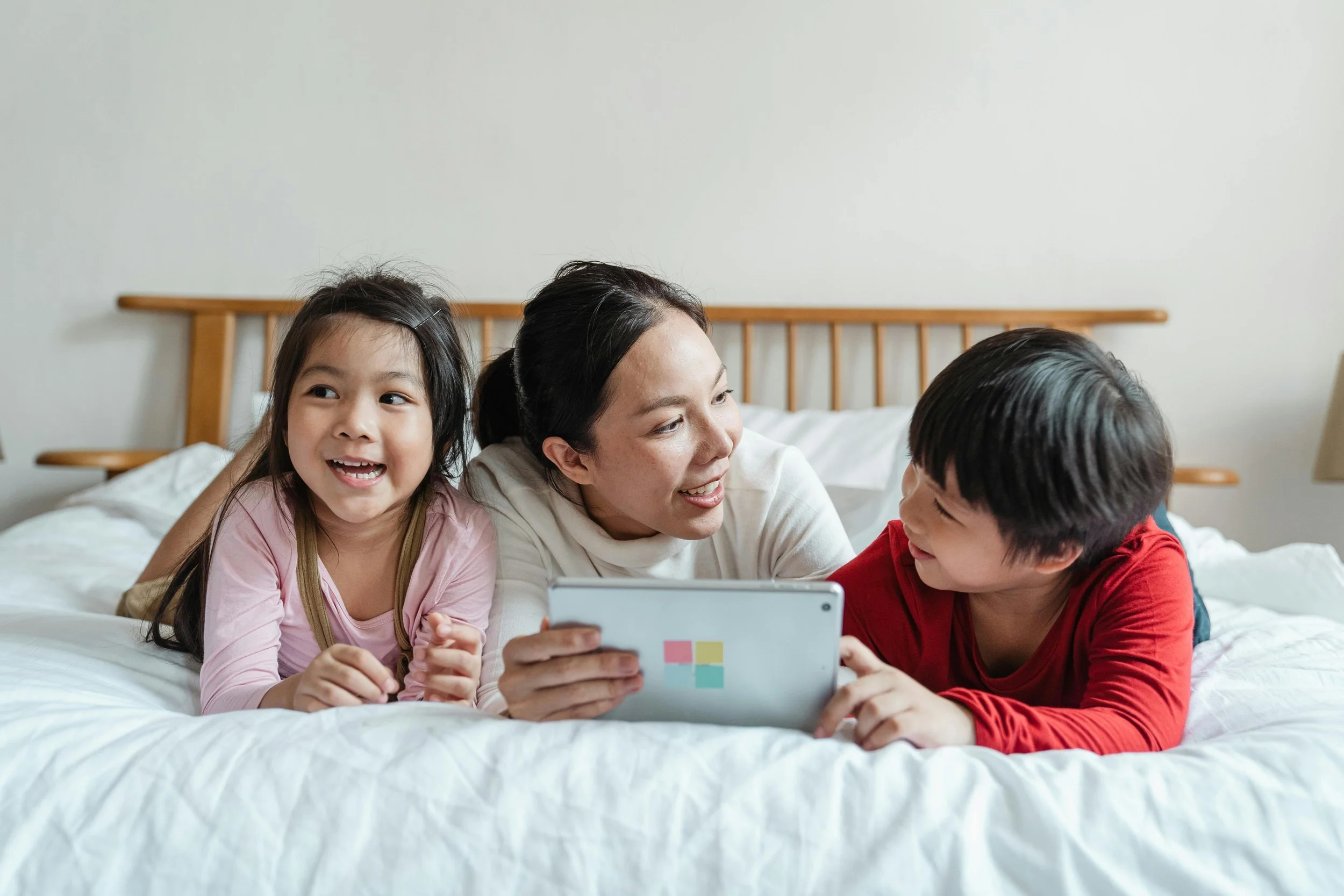 A learning coach lays on a bed with her two students and a tablet
