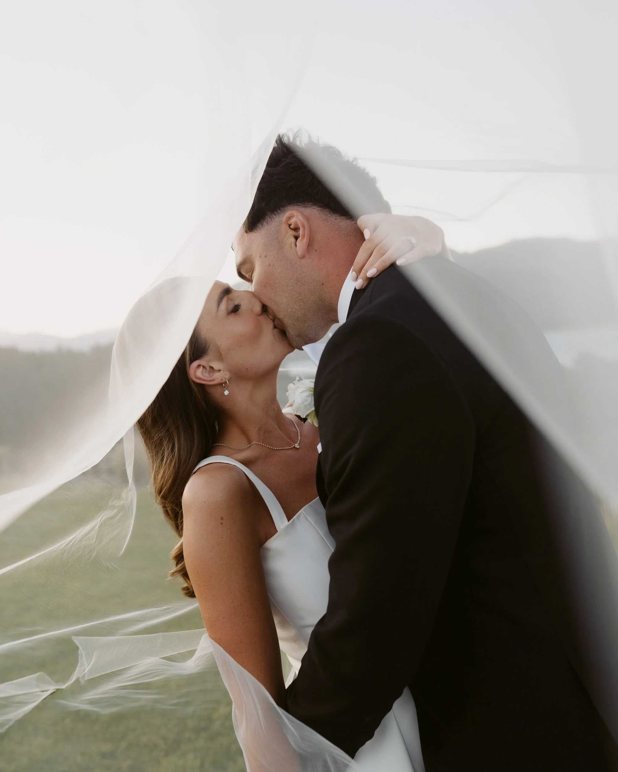 David and Lucy kissing under her veil, Lucy wearing the HoneyBelle Coco Necklace with a natural diamond and diamond drop earrings