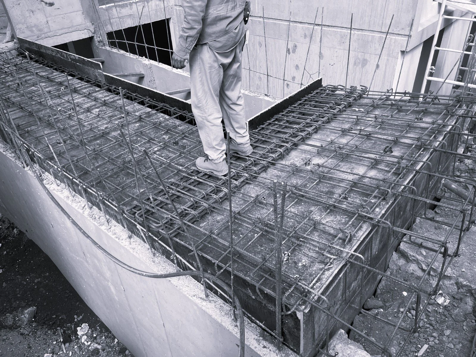Obrero de construcción sobre una estructura de refuerzo de acero para una base de concreto en construcción.