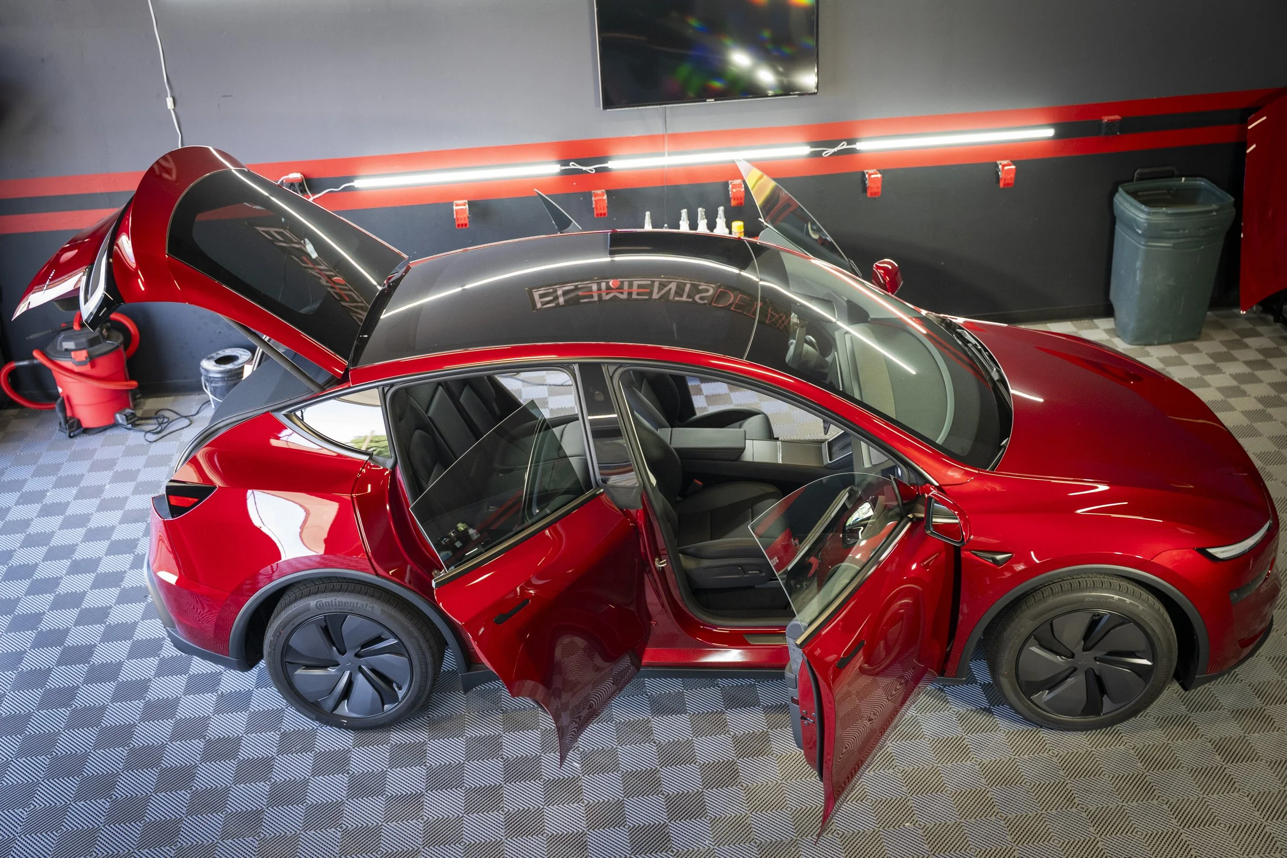 Red Tesla with black wheels, black side mirrors, and a rear wing spoiler.