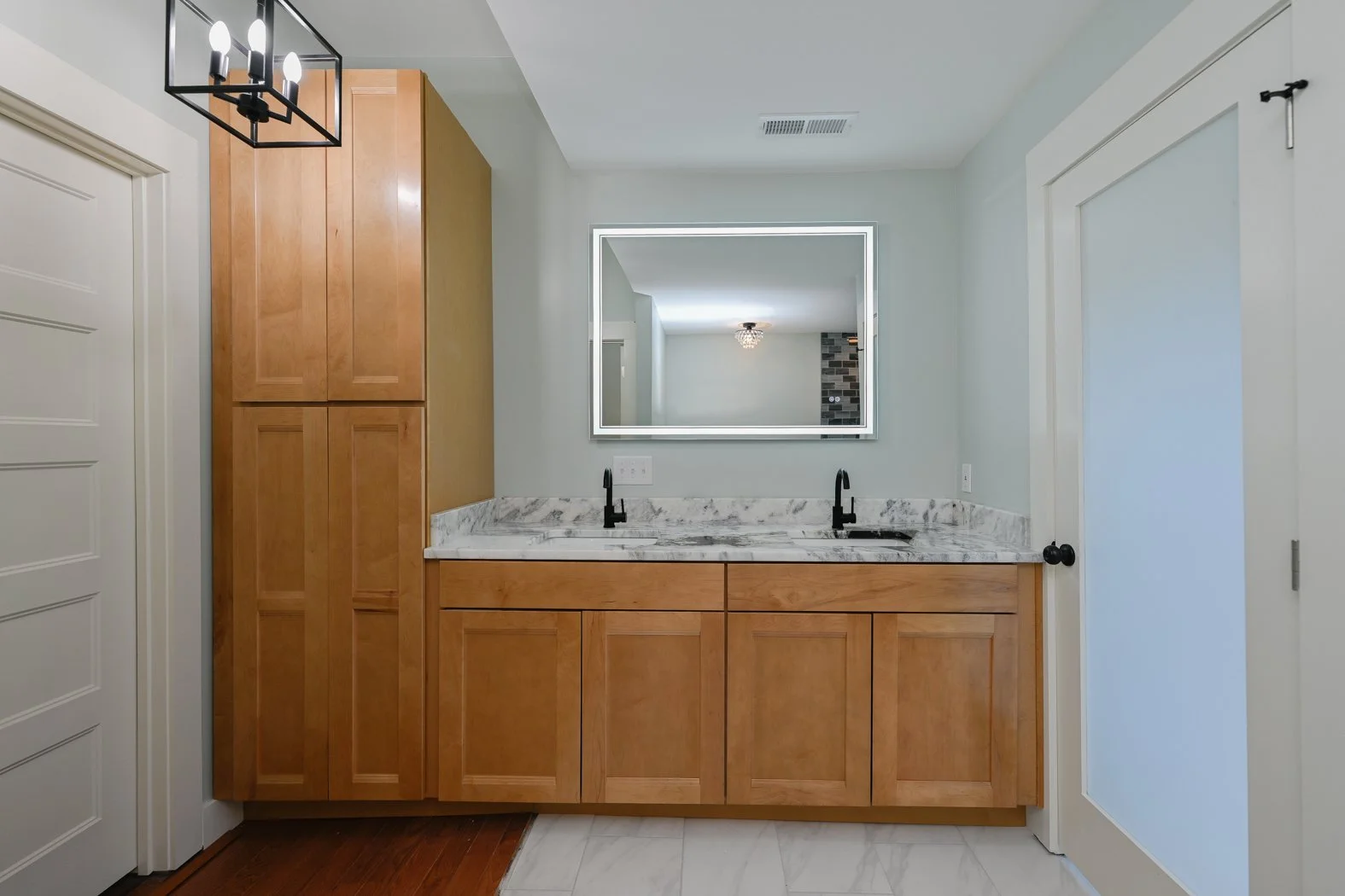 Renovated primary bathroom at 1334 Jameson Road in Easley, SC, featuring a double-sink vanity, natural wood cabinetry, marble-look countertops, matte black faucets, and built-in storage.