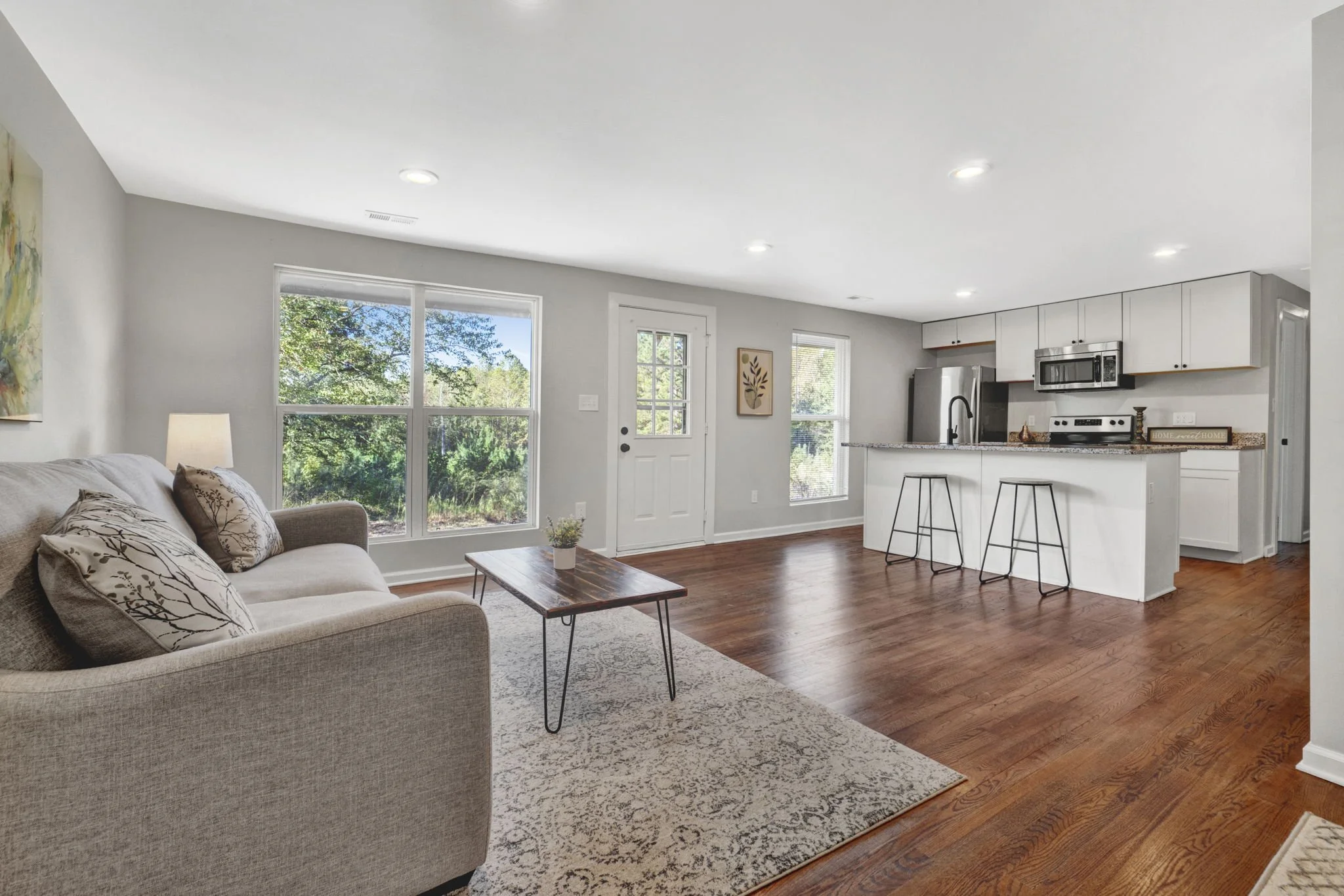 Renovated living room at 1317 Hub Wilson Road in Landrum, SC, featuring hardwood floors, large windows, and an open-concept kitchen with breakfast bar seating.