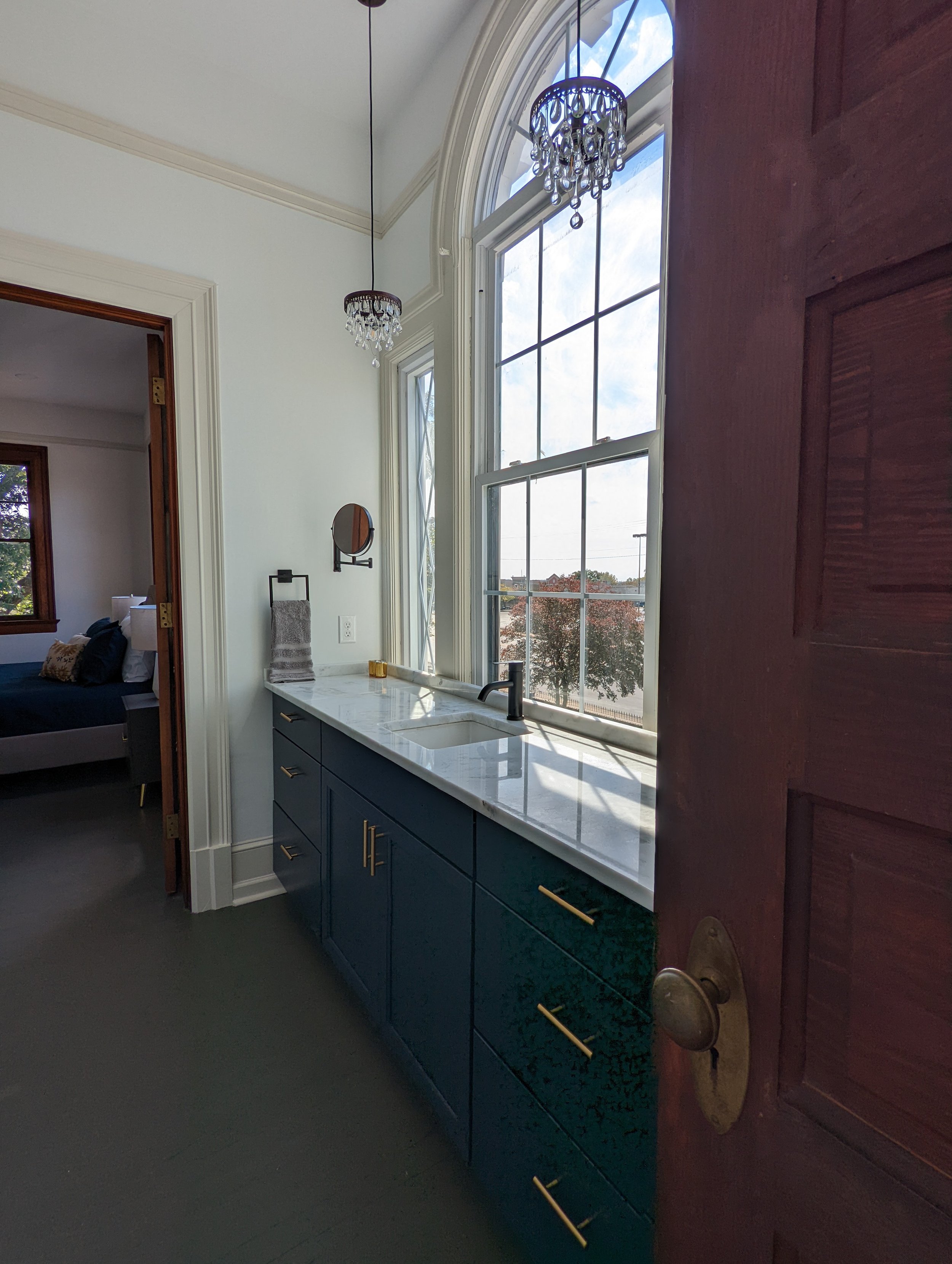 Renovated bathroom at Historic Hampton House 1908 in Pickens, SC, featuring a navy blue vanity, white marble countertop, black faucet, and large windows overlooking the grounds.