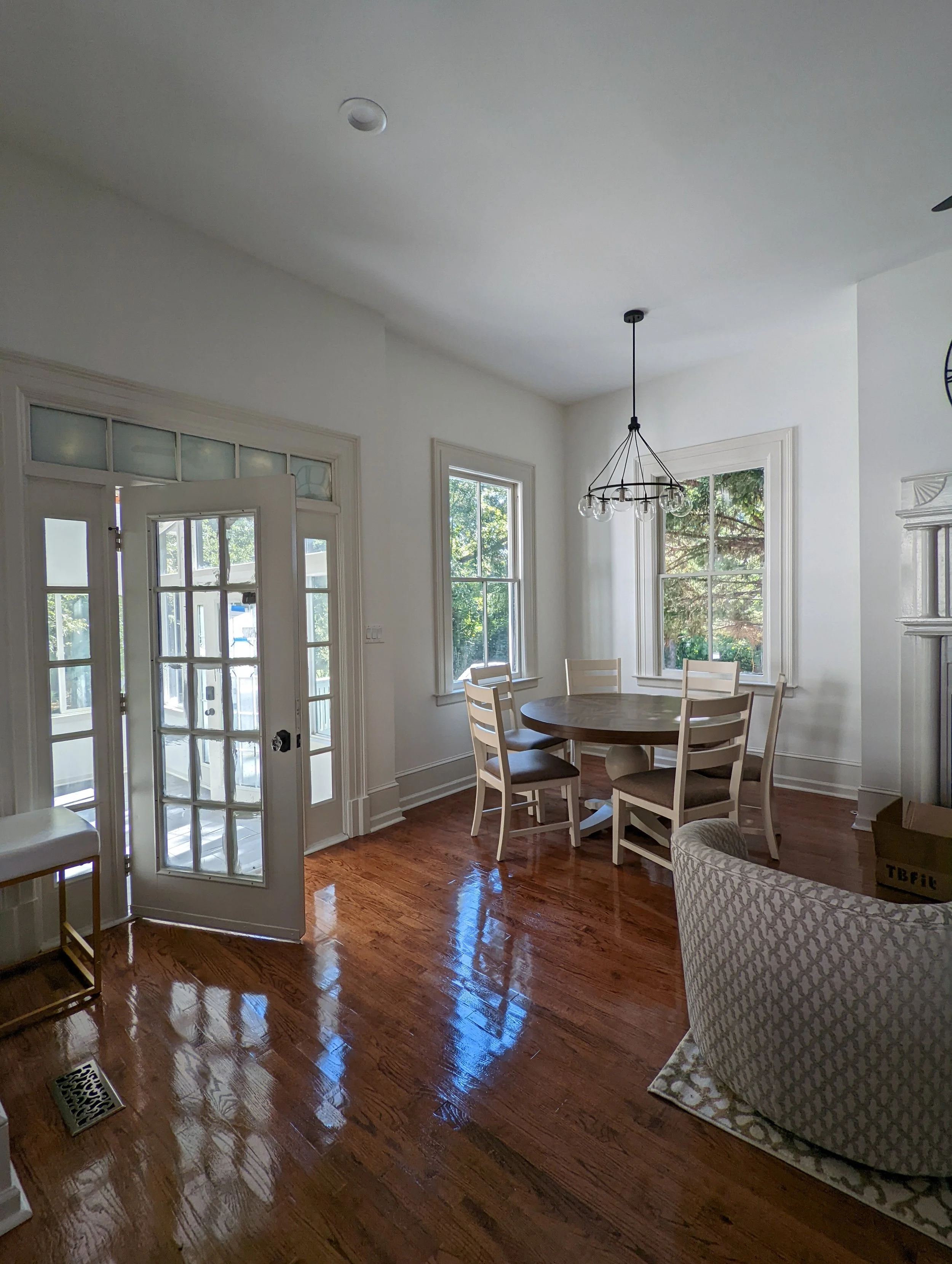 Renovated dining area at Historic Hampton House 1908 in Pickens, SC, featuring French doors, large windows, original wood flooring, and a round dining table beneath a modern chandelier.