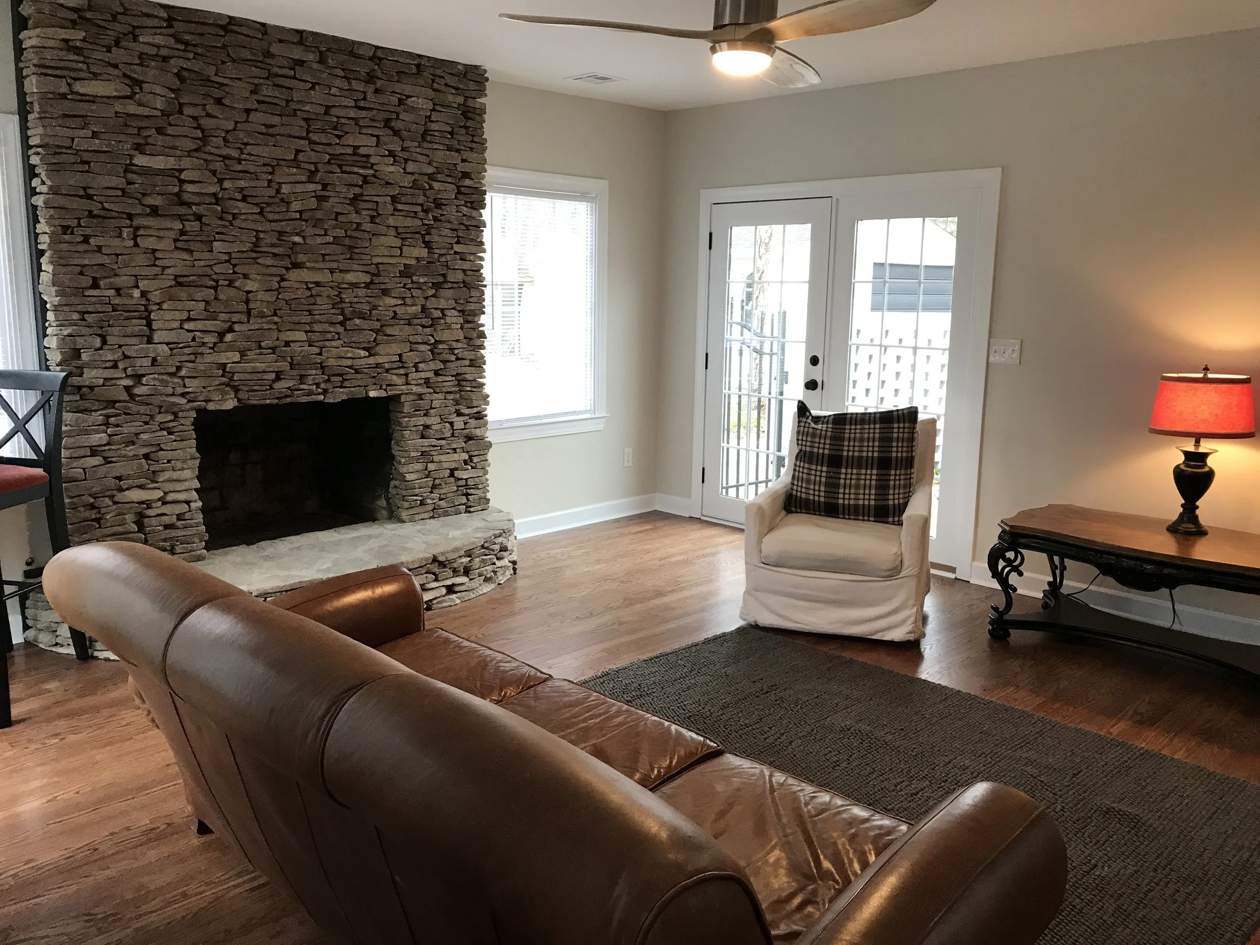 Renovated living room at 104 Medallion Lane in Lyman, SC, featuring a floor-to-ceiling stone fireplace, original hardwood floors, and French doors opening to a private courtyard.