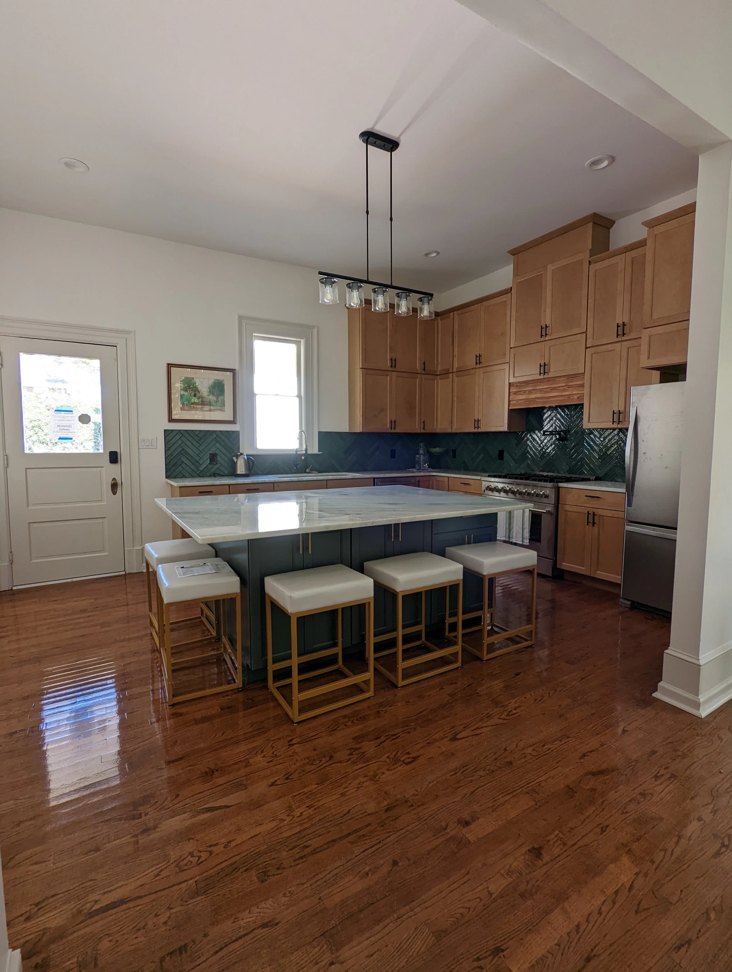 Renovated kitchen at Historic Hampton House 1908 in Pickens, SC, featuring natural wood cabinetry, dark green herringbone tile backsplash, marble countertops, and a large central island with seating.