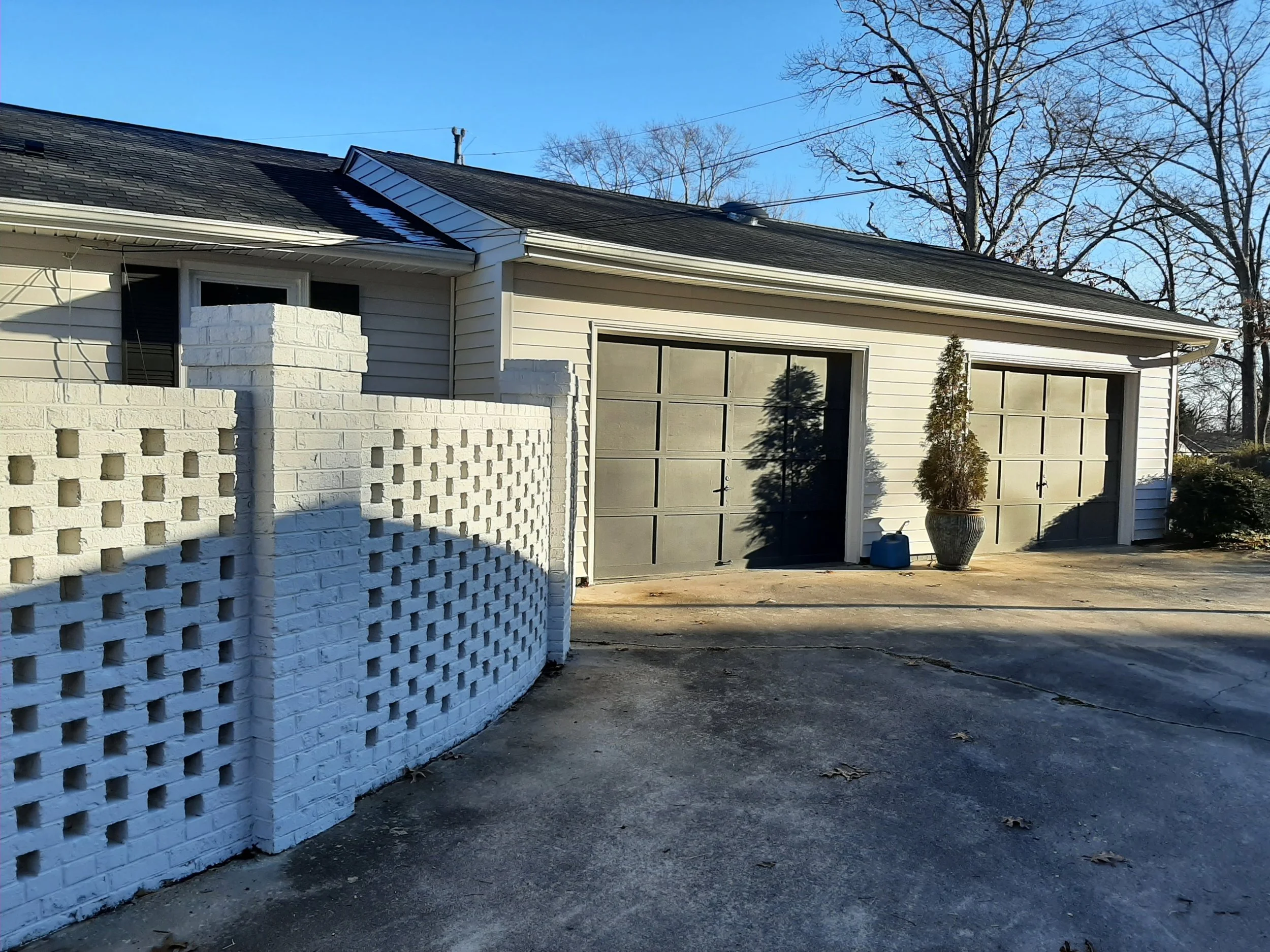Attached two-car garage at 104 Medallion Lane in Lyman, SC, featuring dark garage doors, white exterior siding, a concrete driveway, and a decorative brick courtyard wall.