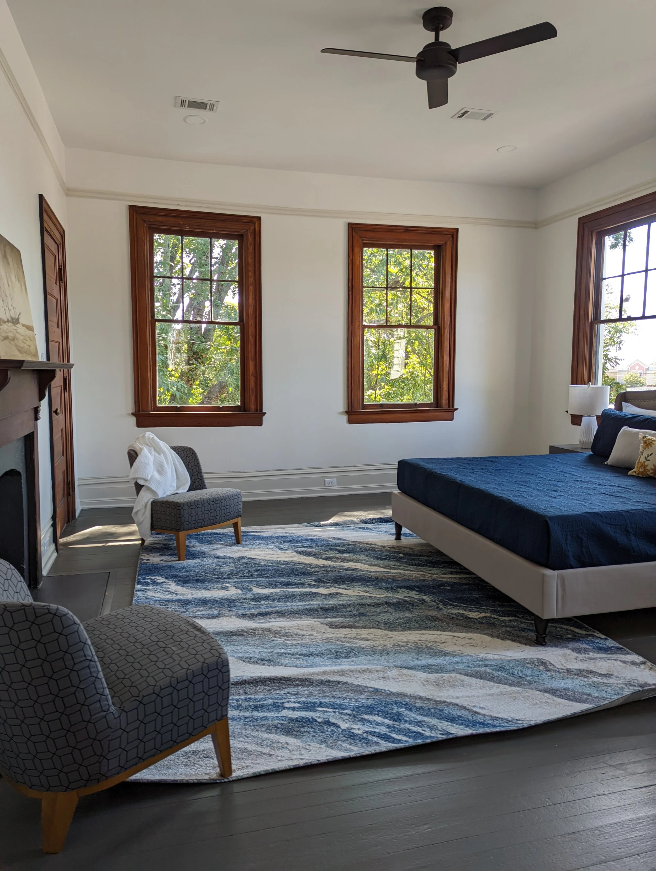 Renovated bedroom at Historic Hampton House 1908 in Pickens, SC, featuring original wood-trimmed windows, a historic fireplace, dark wood flooring, and contemporary furnishings.
