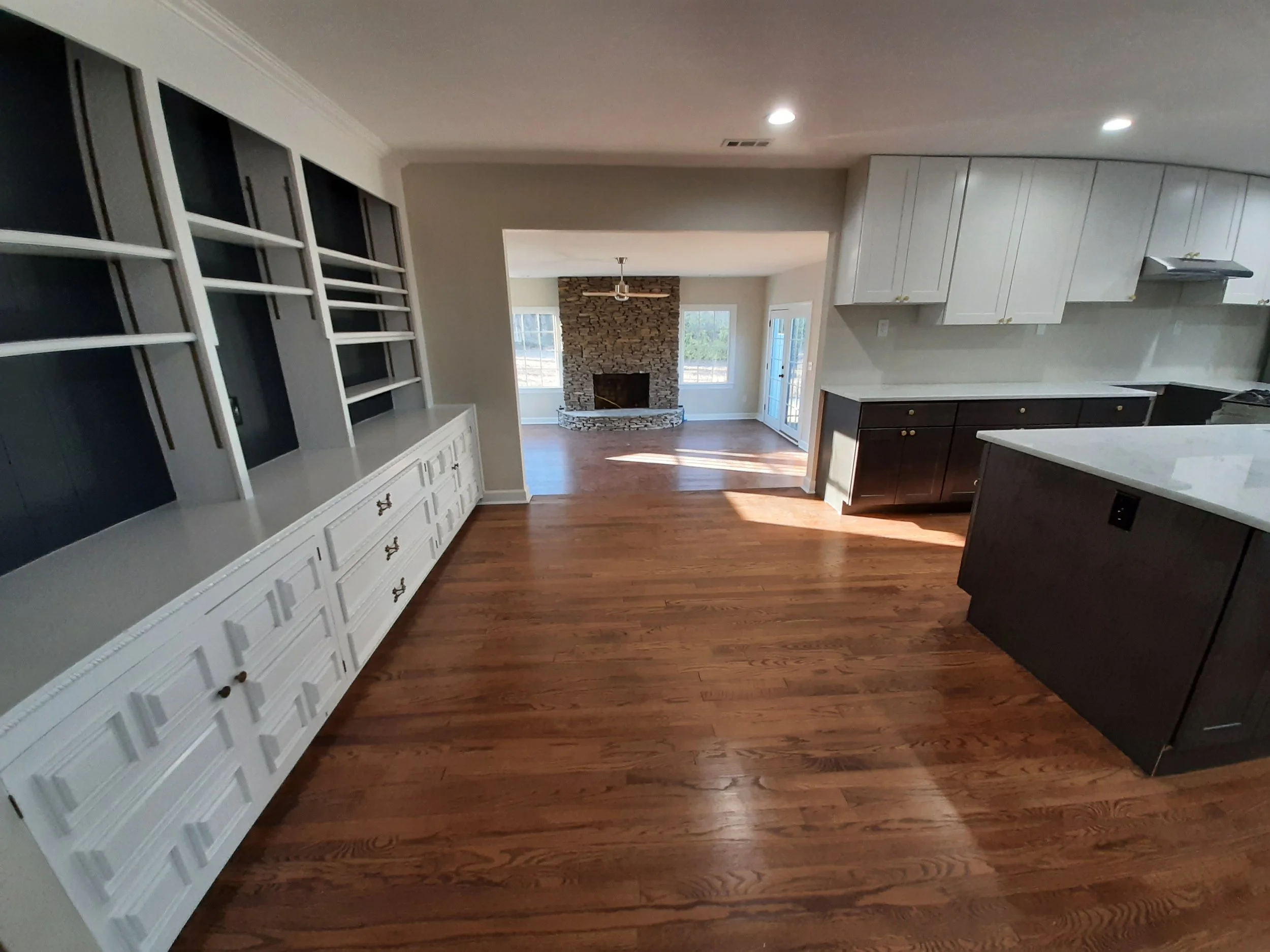 Renovated kitchen and living area at 104 Medallion Lane in Lyman, SC, featuring custom built-in shelving, original hardwood floors, two-tone cabinetry, and a floor-to-ceiling stone fireplace.