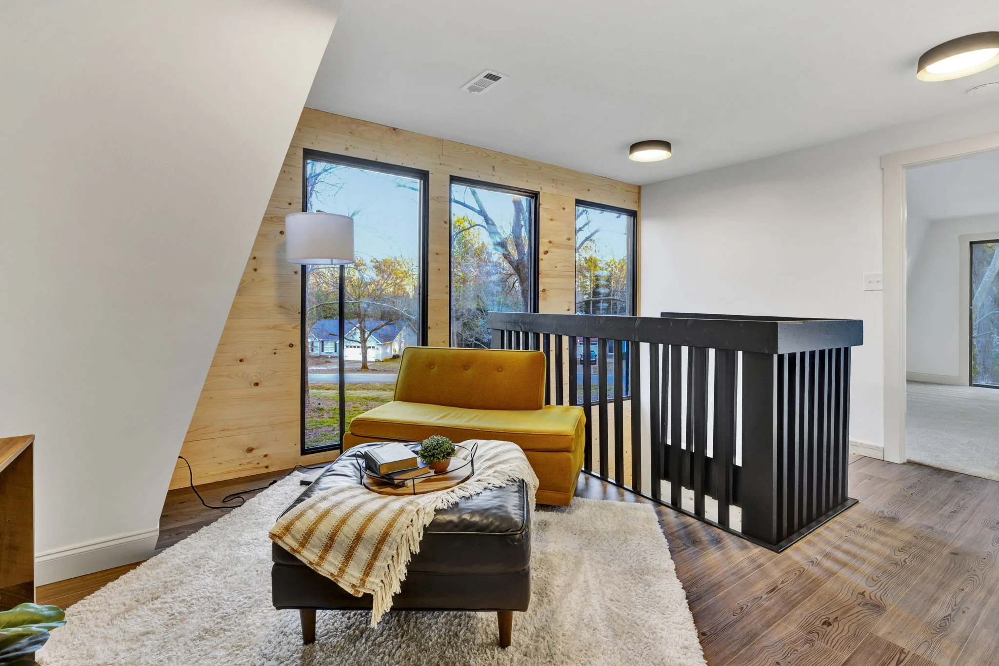 Renovated upstairs loft at 112 Wayland Drive in Duncan, SC, featuring floor-to-ceiling windows, natural wood accent walls, black stair railings, and a cozy sitting area.